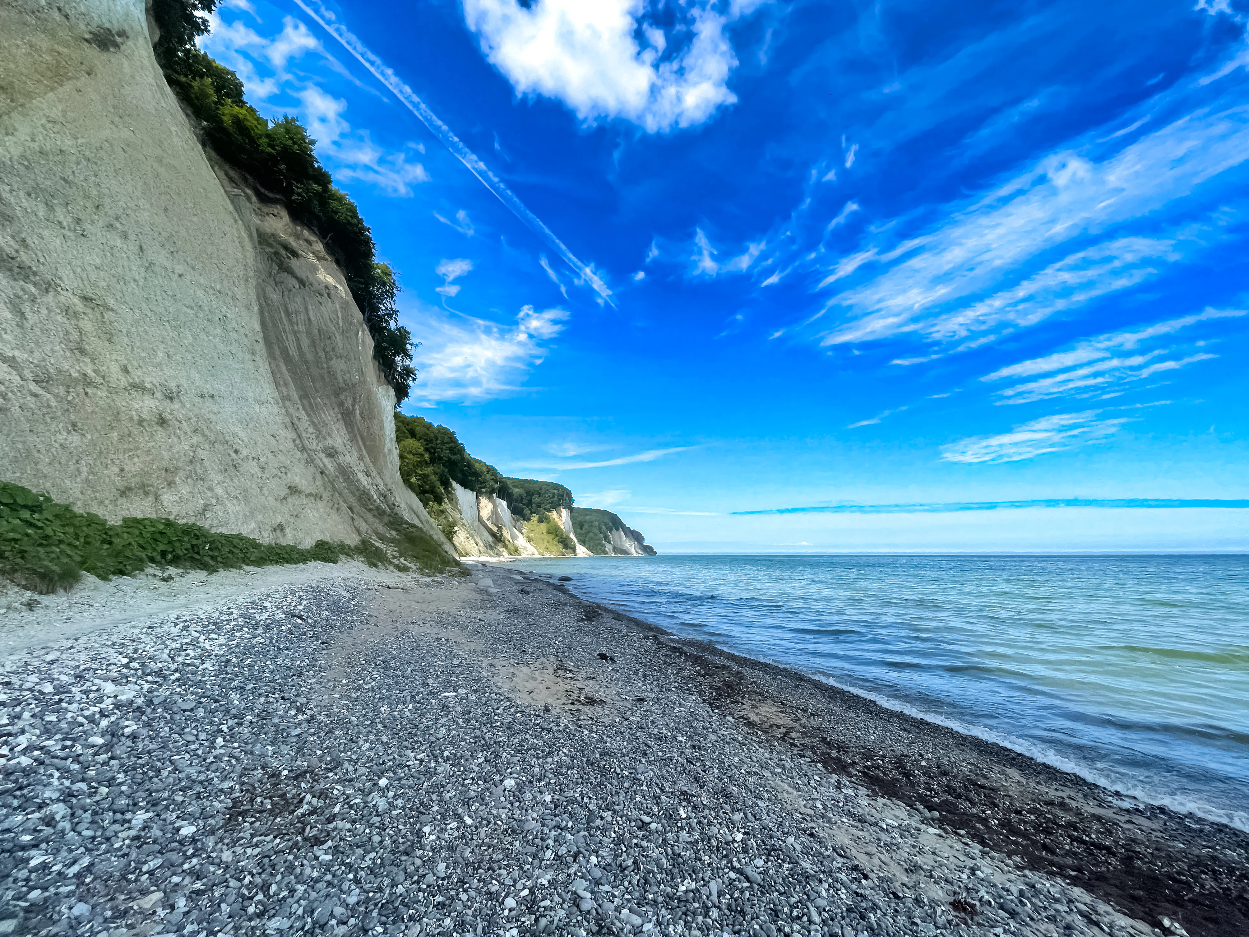 Pebbled beach along the coast with white chalk cliffs under a blue sky