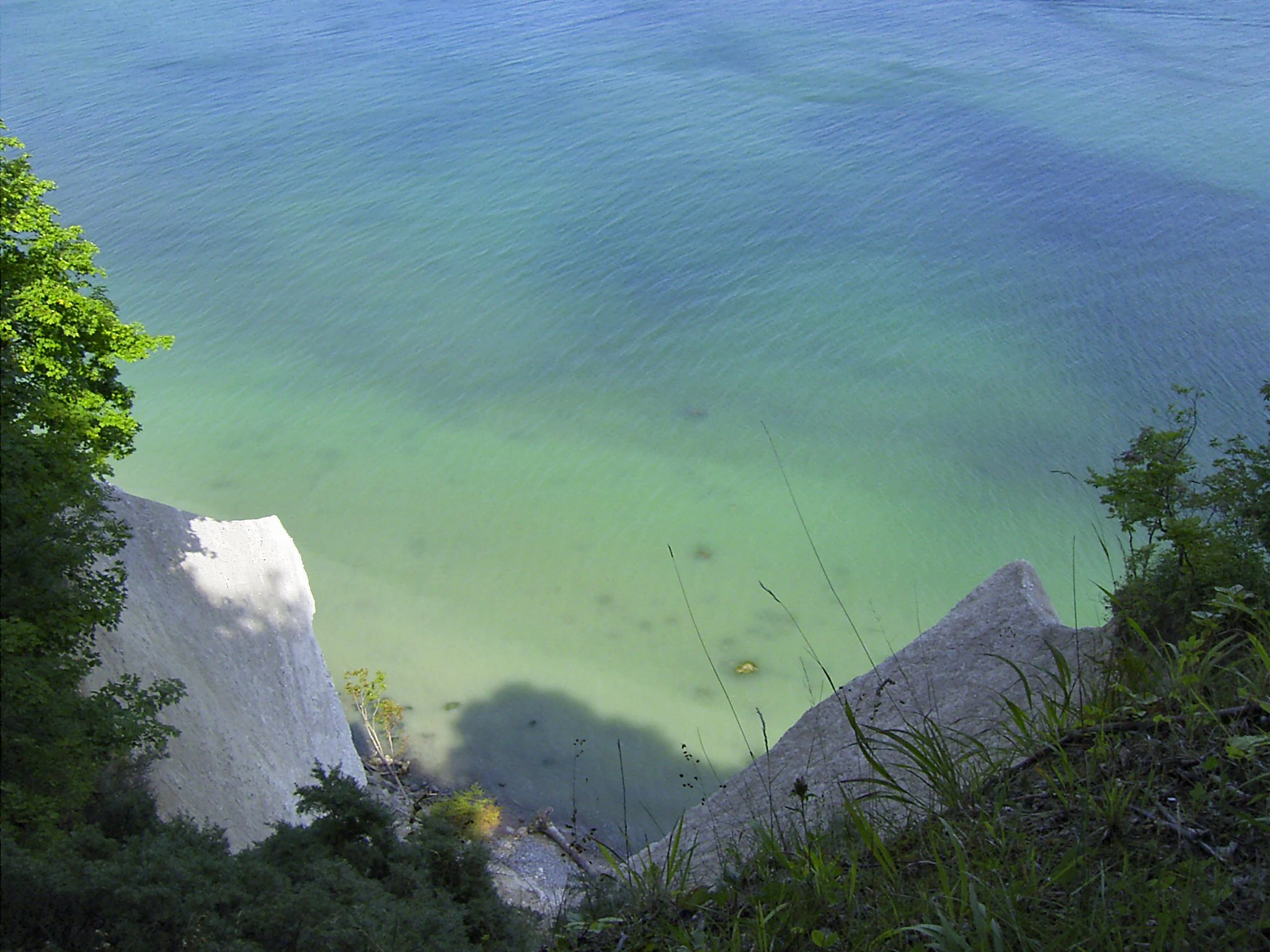 Chalk cliffs overlooking turquoise sea with green vegetation on the sides
