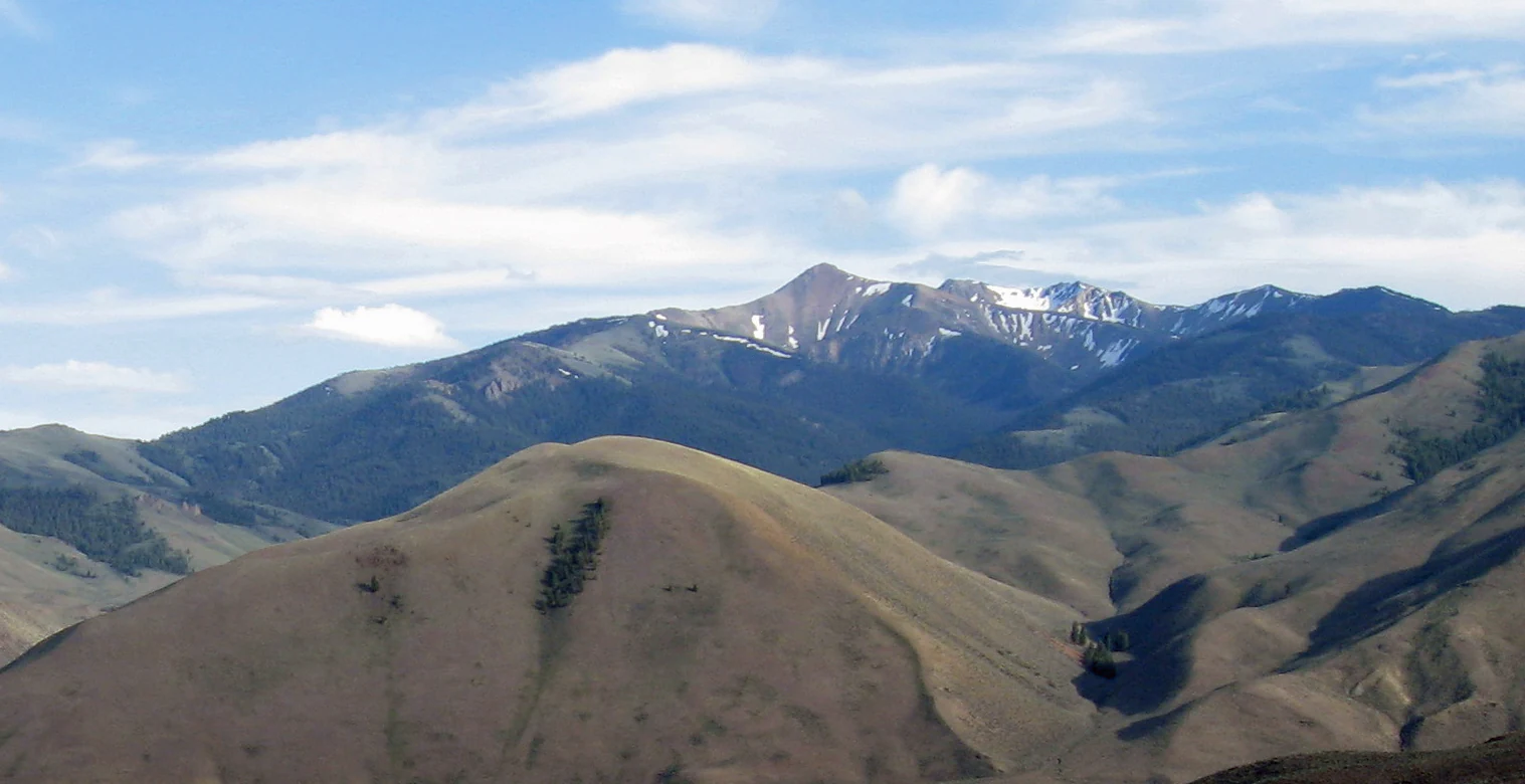A wide view of the rugged, dry-grass mountain slopes of Sheep Mountain in the Jim McClure, Jerry Peak Wilderness, under a blue sky with light clouds.