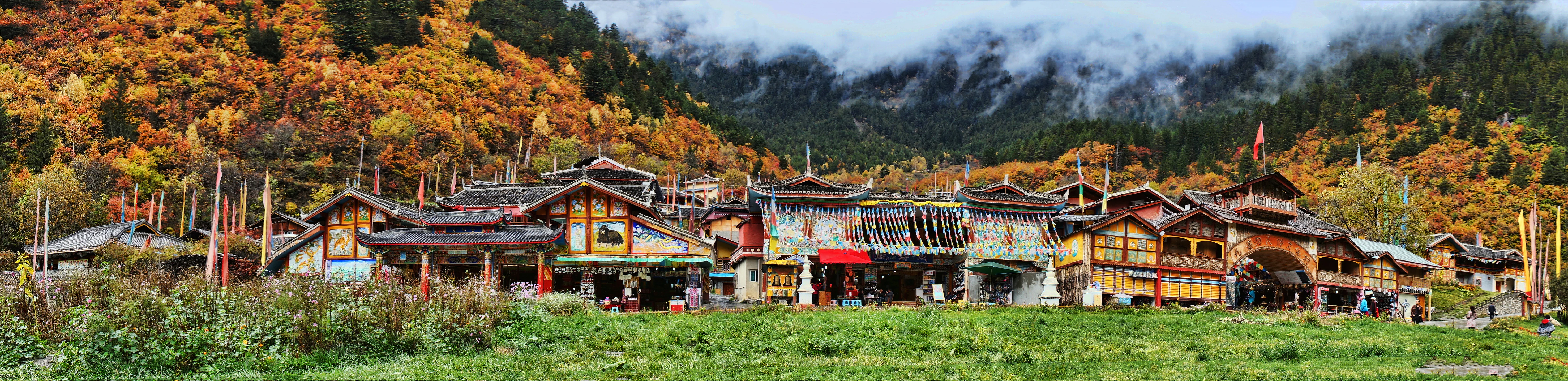 Panoramic view of traditional wooden buildings in Shuzheng Village at the base of a forested mountain slope in autumn.