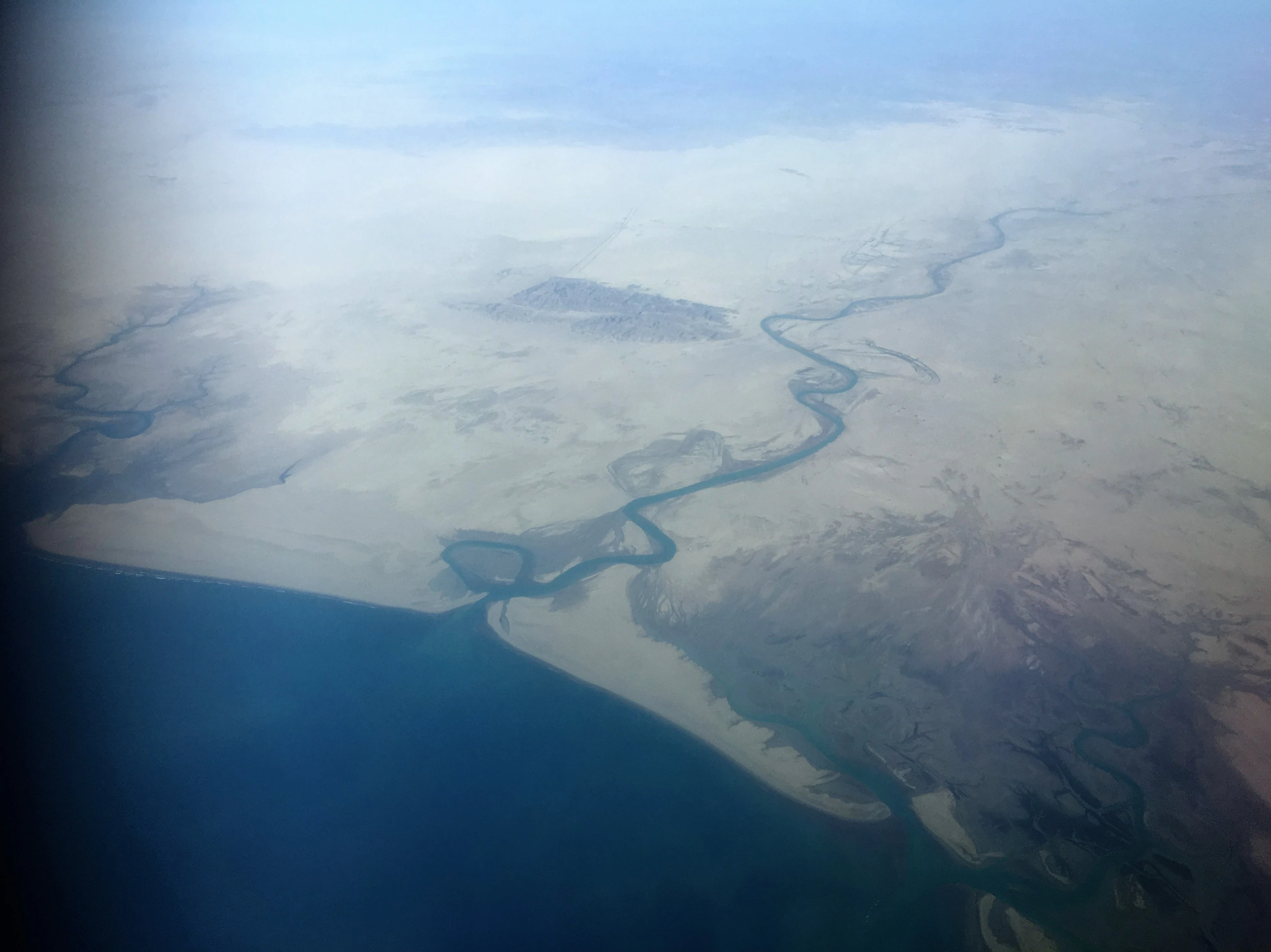 Fotografía aérea que muestra un río serpenteante que fluye a través de un paisaje costero árido y plano hacia las aguas azul profundo del mar.