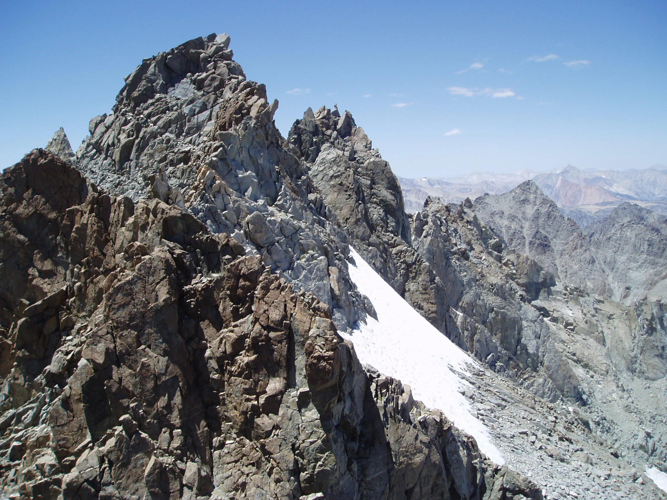 A high angle view of jagged, rocky mountain peaks with a patch of snow visible on the steep slope.