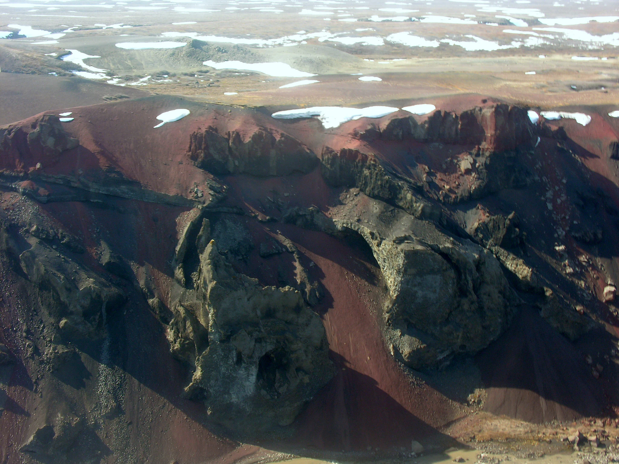 Aerial view of a rugged canyon with rocky terrain, patches of snow, and a river winding through the landscape