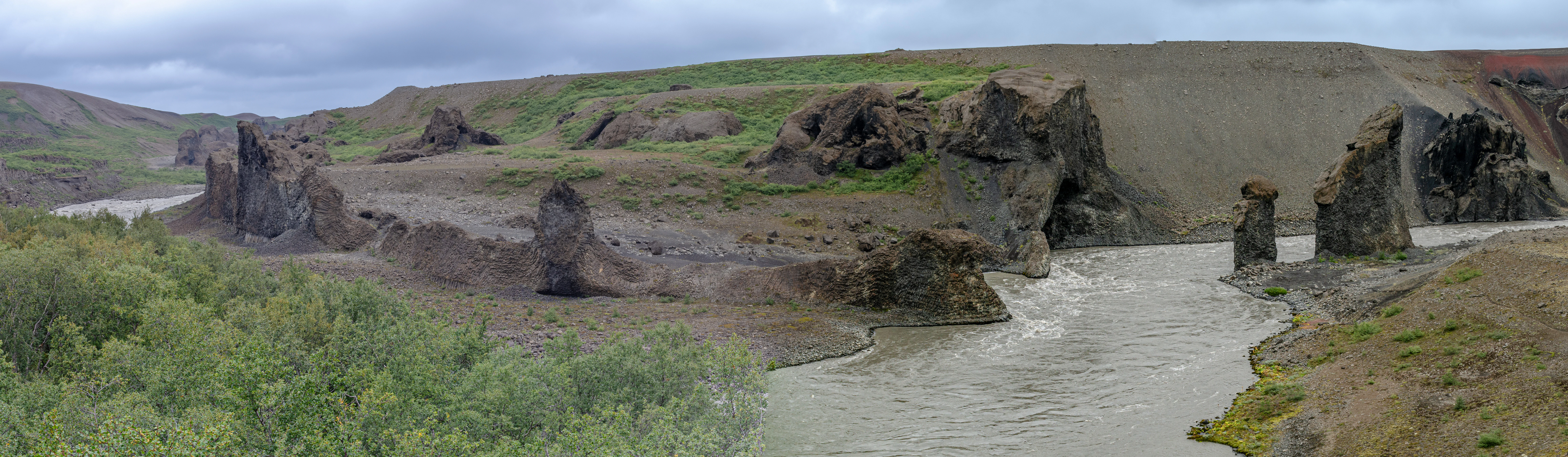River flowing through a canyon with distinctive rock formations and green vegetation under a cloudy sky