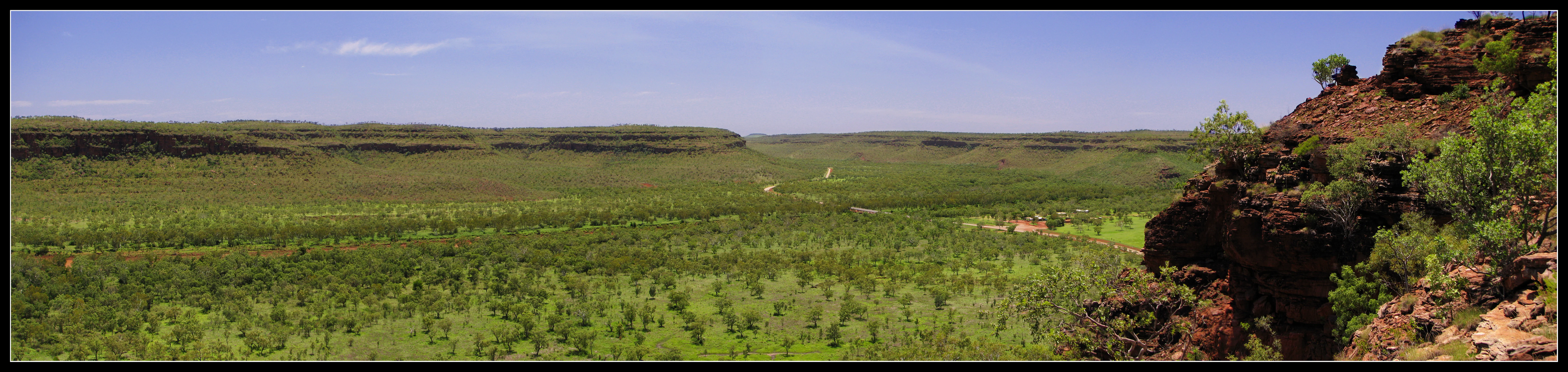 Wide panoramic view of a grassy plain with low hills in the distance and a rocky outcrop on the right side under a clear blue sky