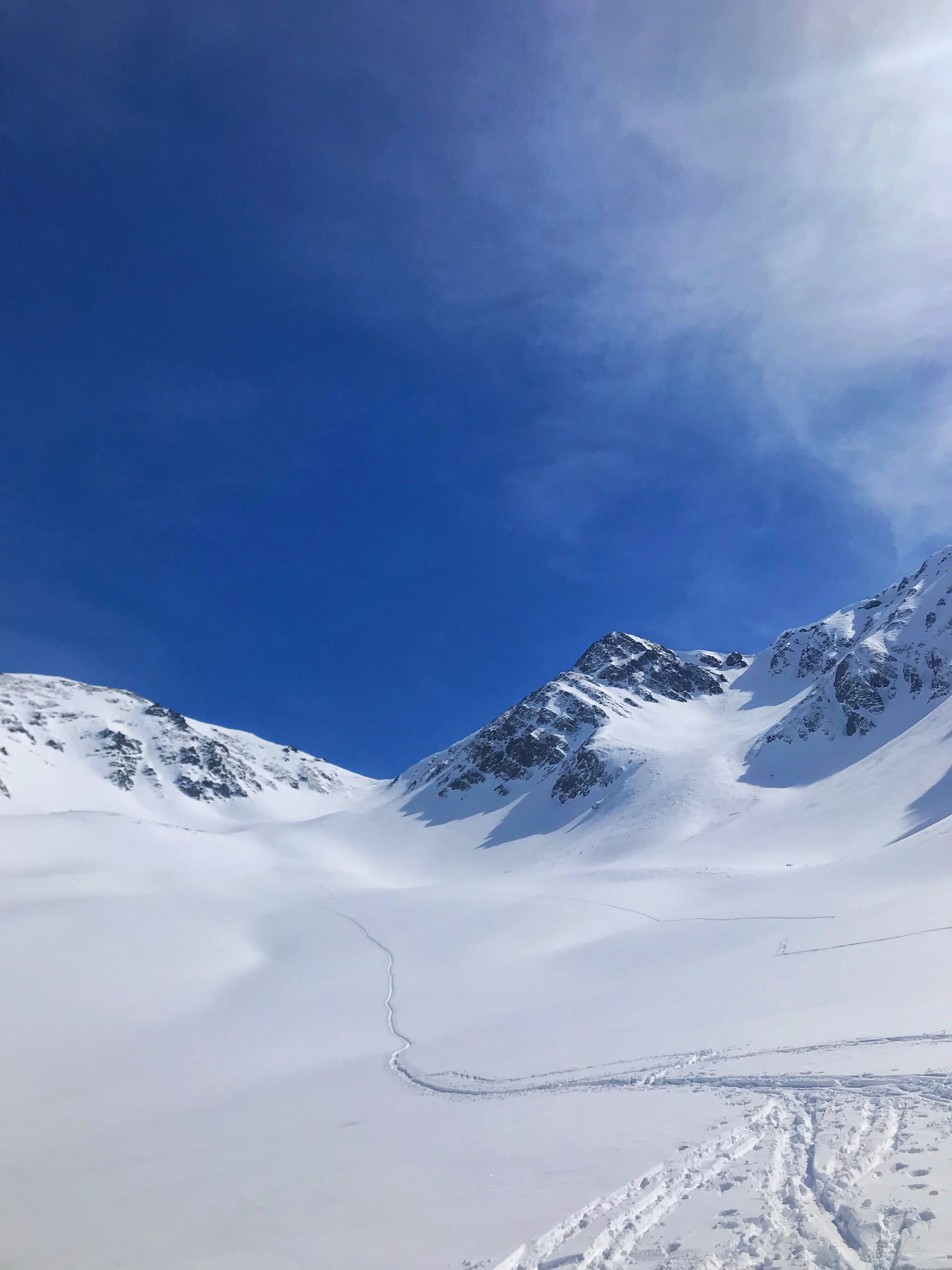Snow-covered mountain peaks and a plateau with visible footprints or tracks under a clear blue sky.
