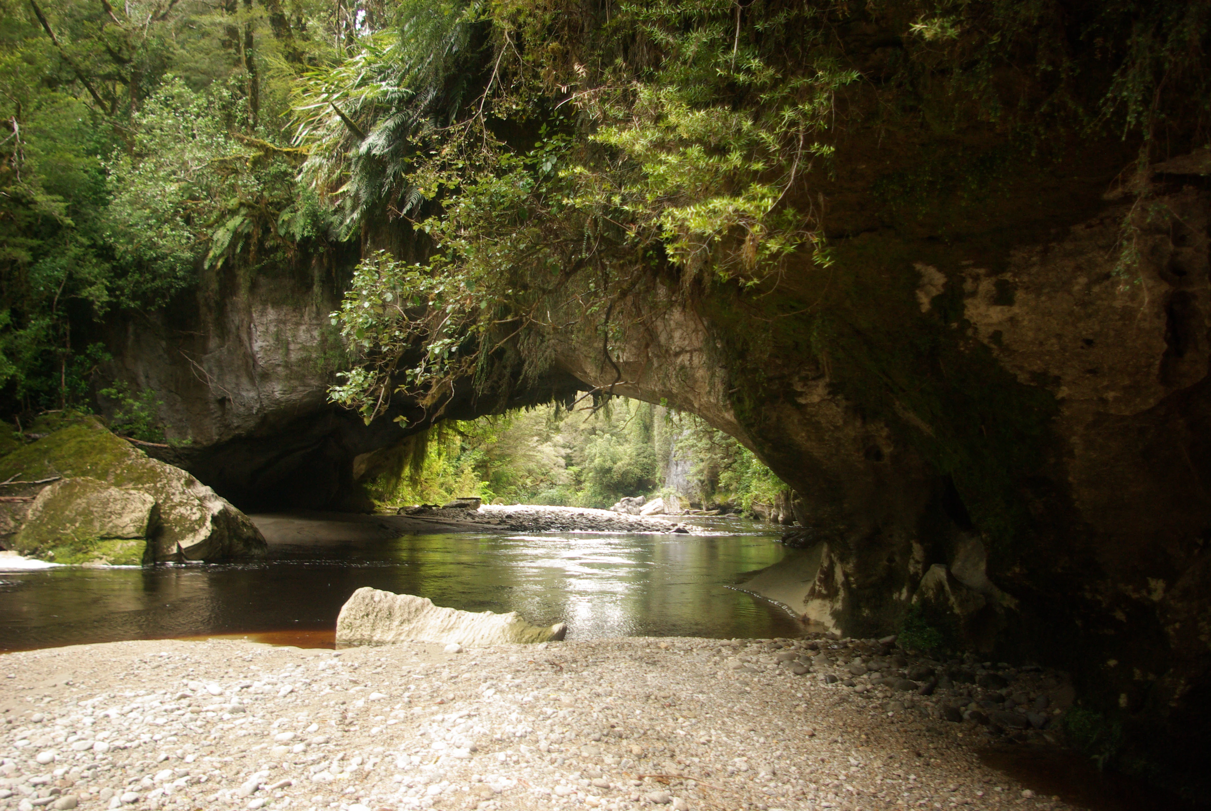 Formación de arco de roca natural que abarca un río tranquilo con fondo boscoso y ribera rocosa