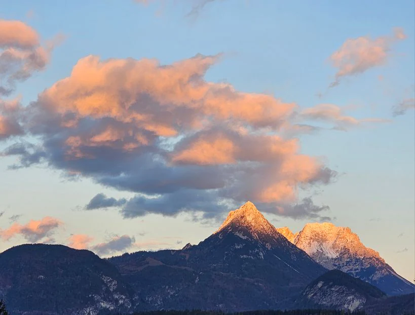 A jagged limestone mountain peak illuminated by the warm, golden light of sunset, set against a blue sky with soft, peach-colored clouds.