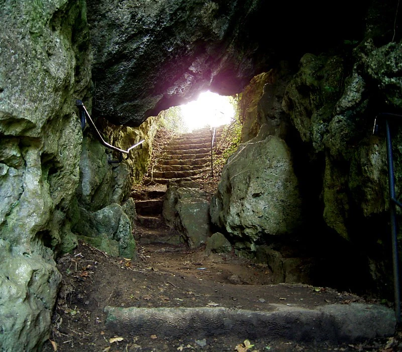 Vista interior de la cueva Kakushöhle mirando hacia la salida luminosa, con un sendero de piedra y escaleras visibles entre grandes paredes de piedra caliza.