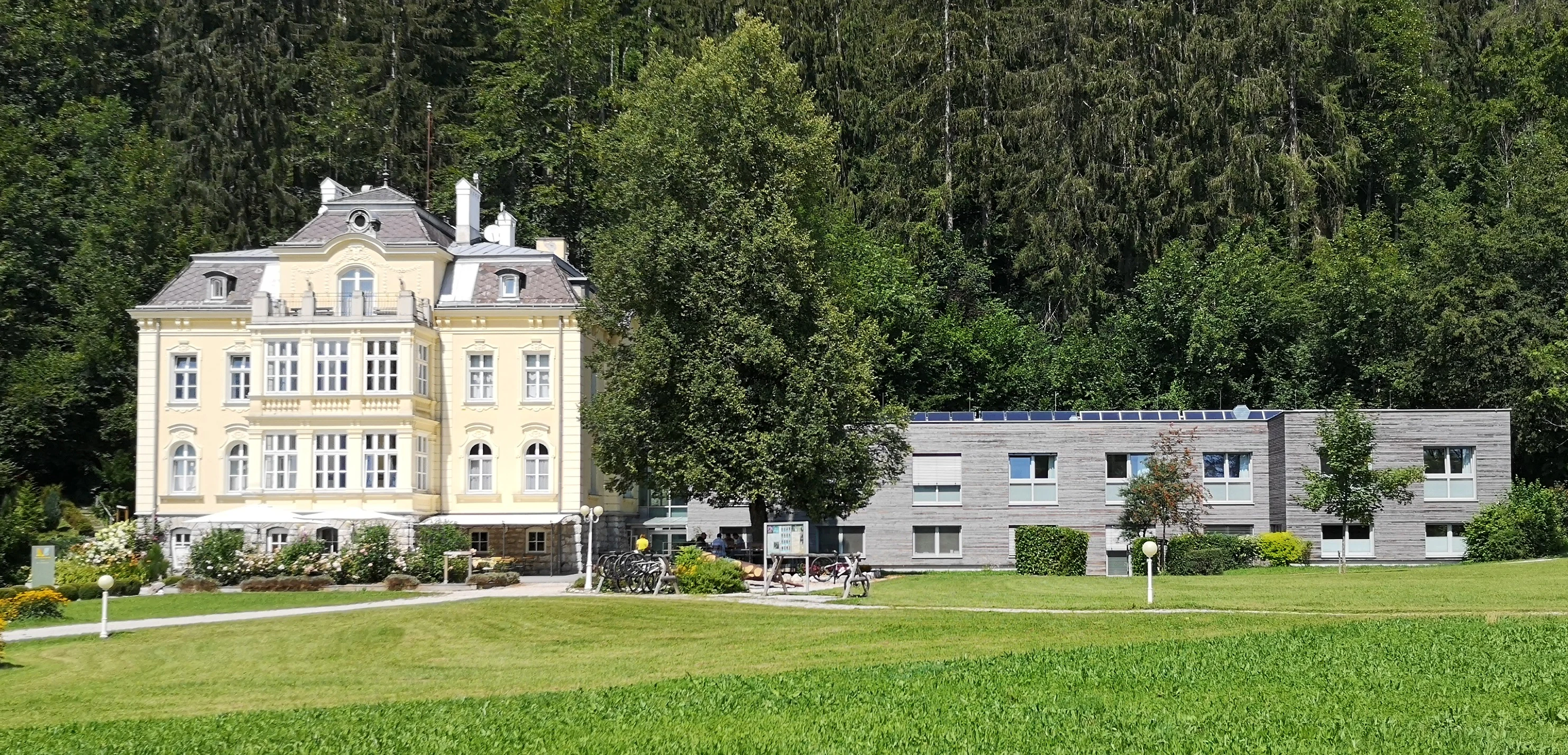 Historic yellow building with white trim and gray roof surrounded by green fields and trees