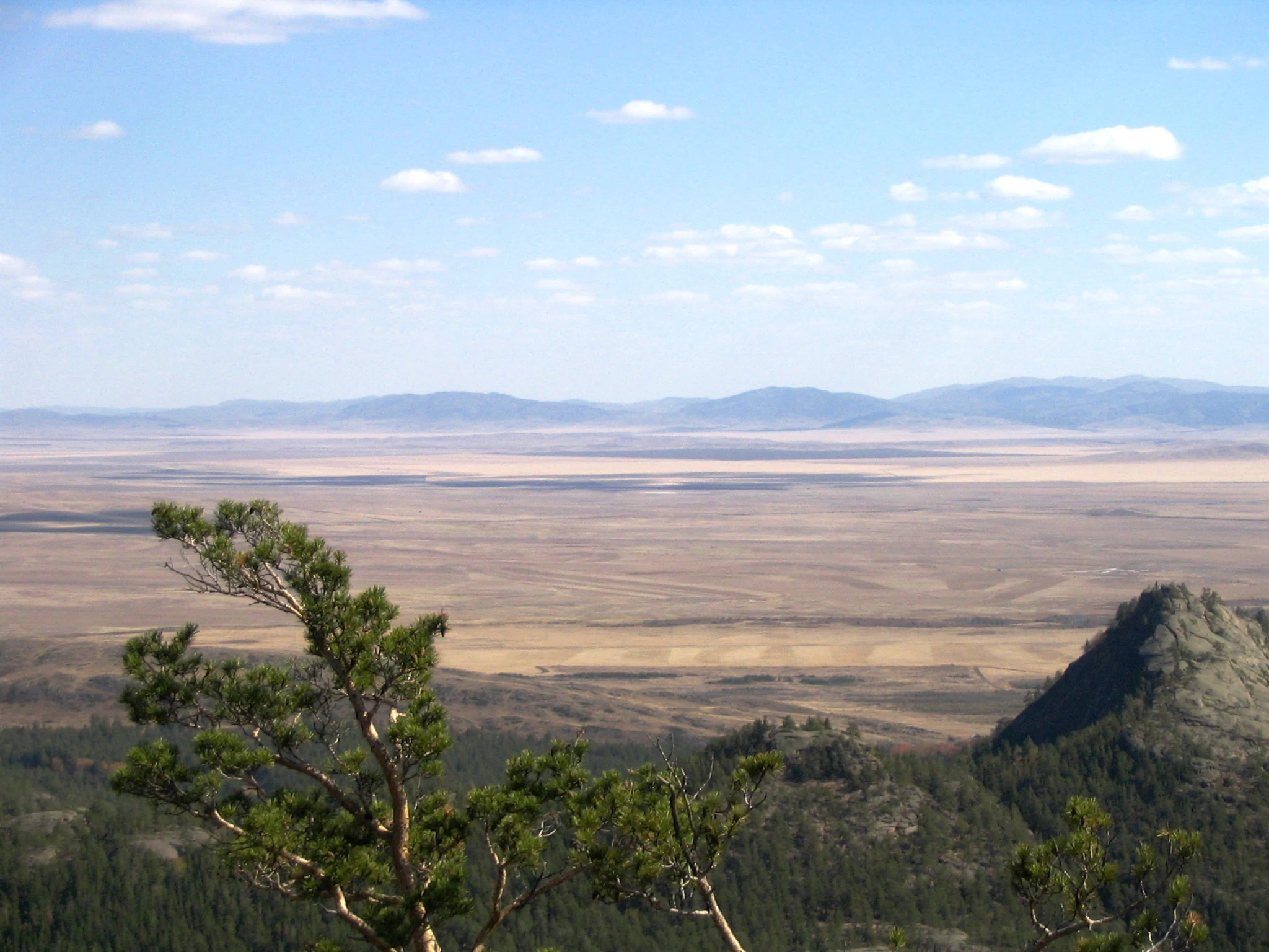 Wide landscape view of mountains, open plain, and scattered trees under a partly cloudy sky.