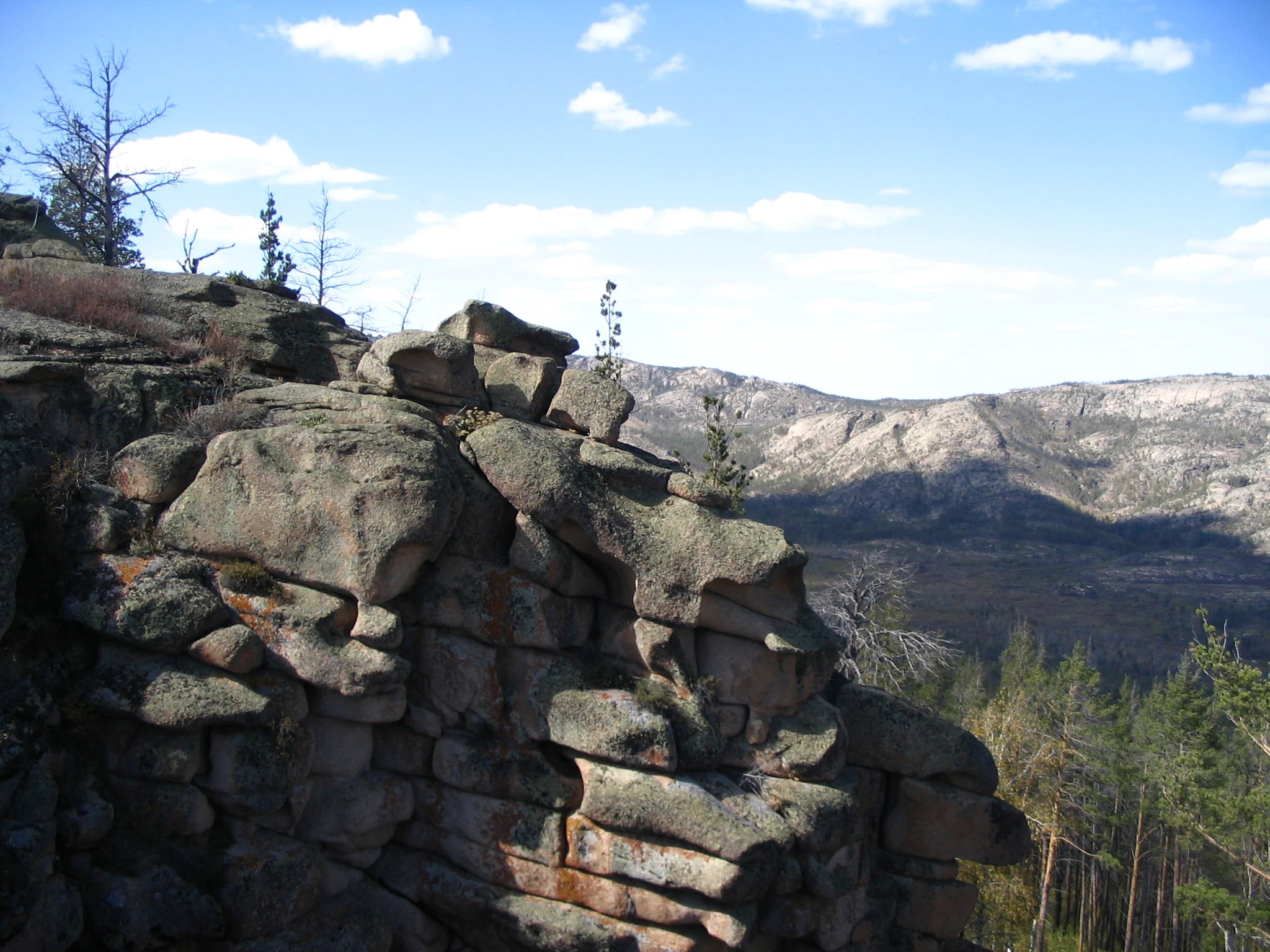 Rocky cliffs and mountain ranges with scattered trees under clear blue sky