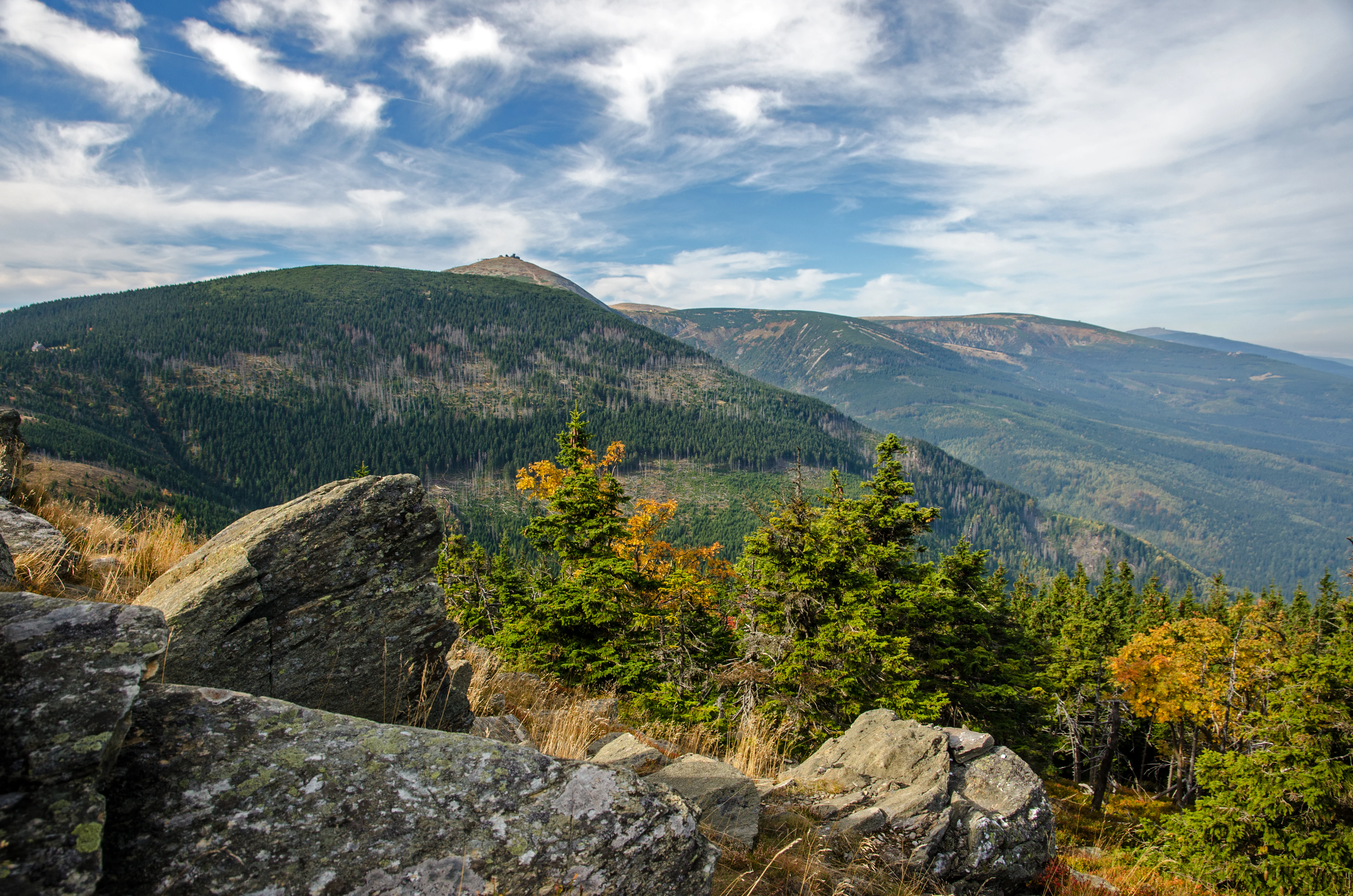 Mountain landscape with rocky outcrops, forested hills, and blue sky with clouds