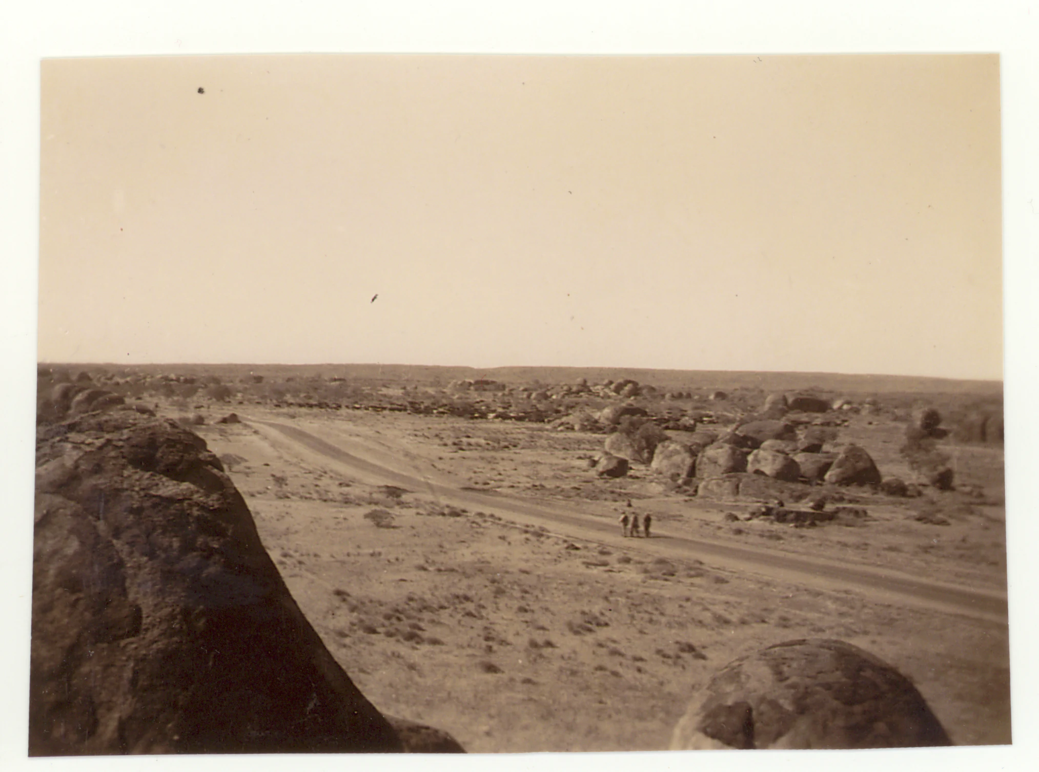 A sepia-toned archival photograph from 1946 showing a vast, dry desert landscape scattered with large, rounded granite boulders and a dirt path with a few small figures walking.