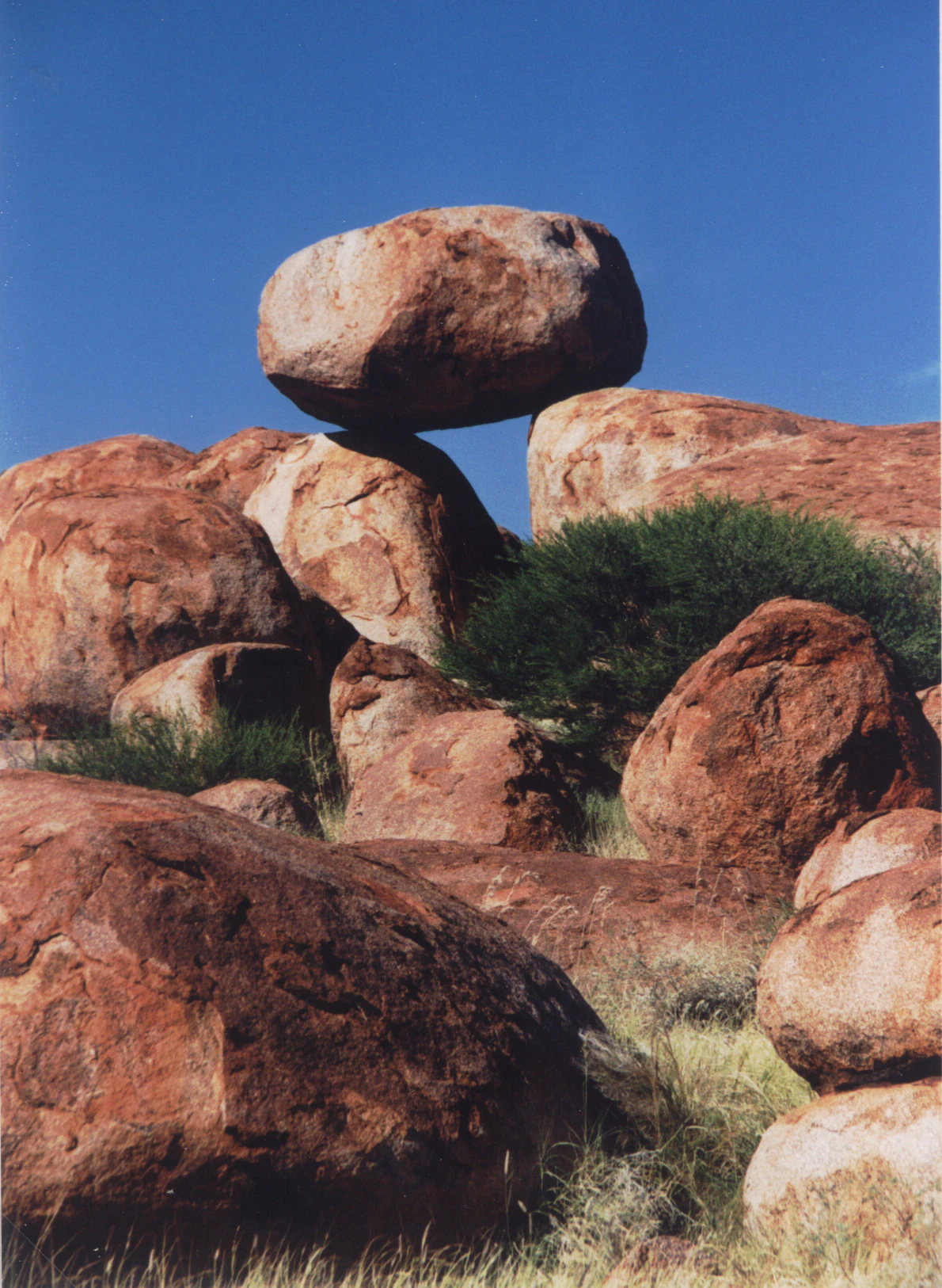 A large, rounded granitic boulder perfectly balanced atop another rock formation at Karlu Karlu, set against a clear blue sky.