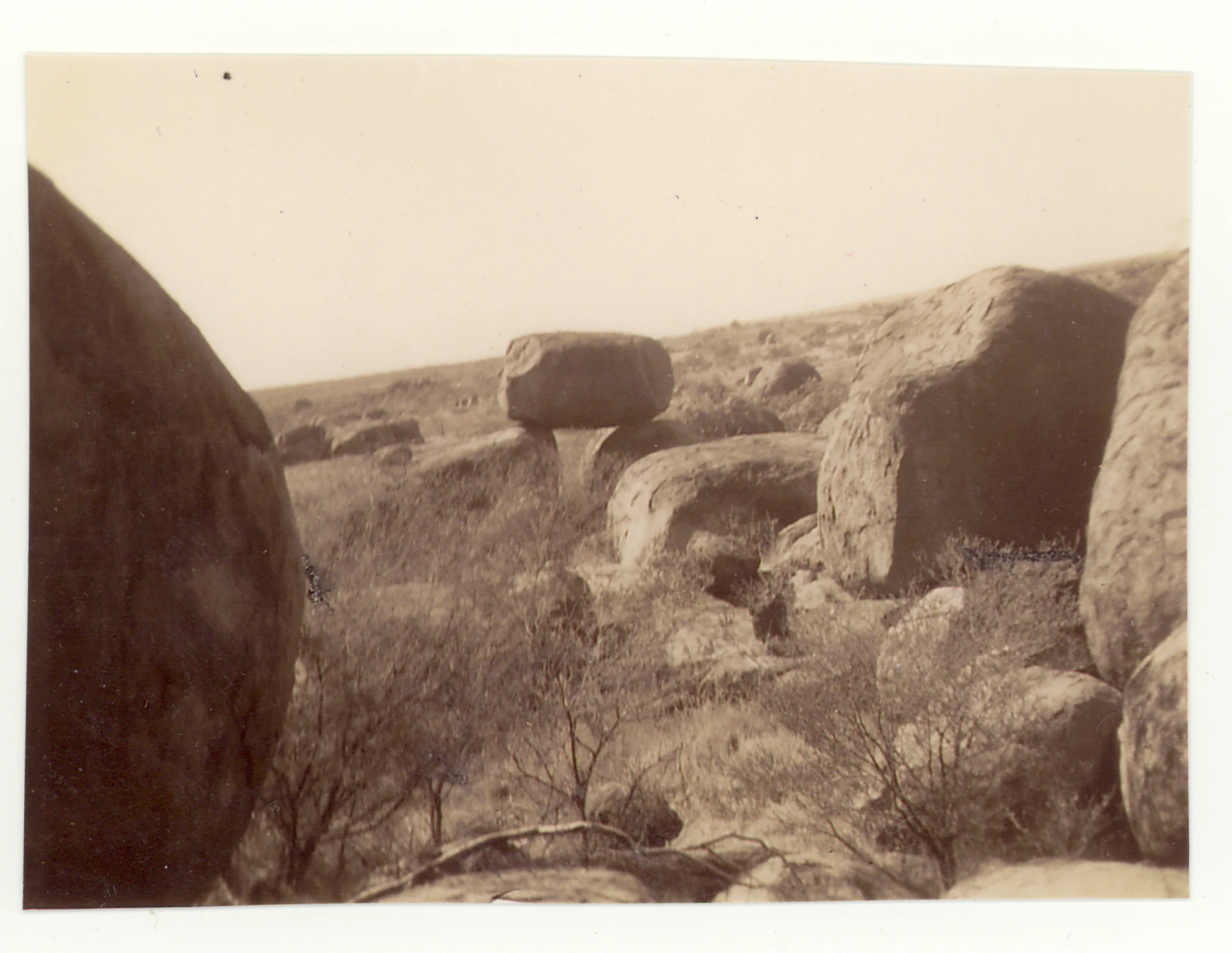 A black and white historic photograph showing large, rounded granite boulders scattered across a dry, arid landscape with sparse low-lying scrub brush.