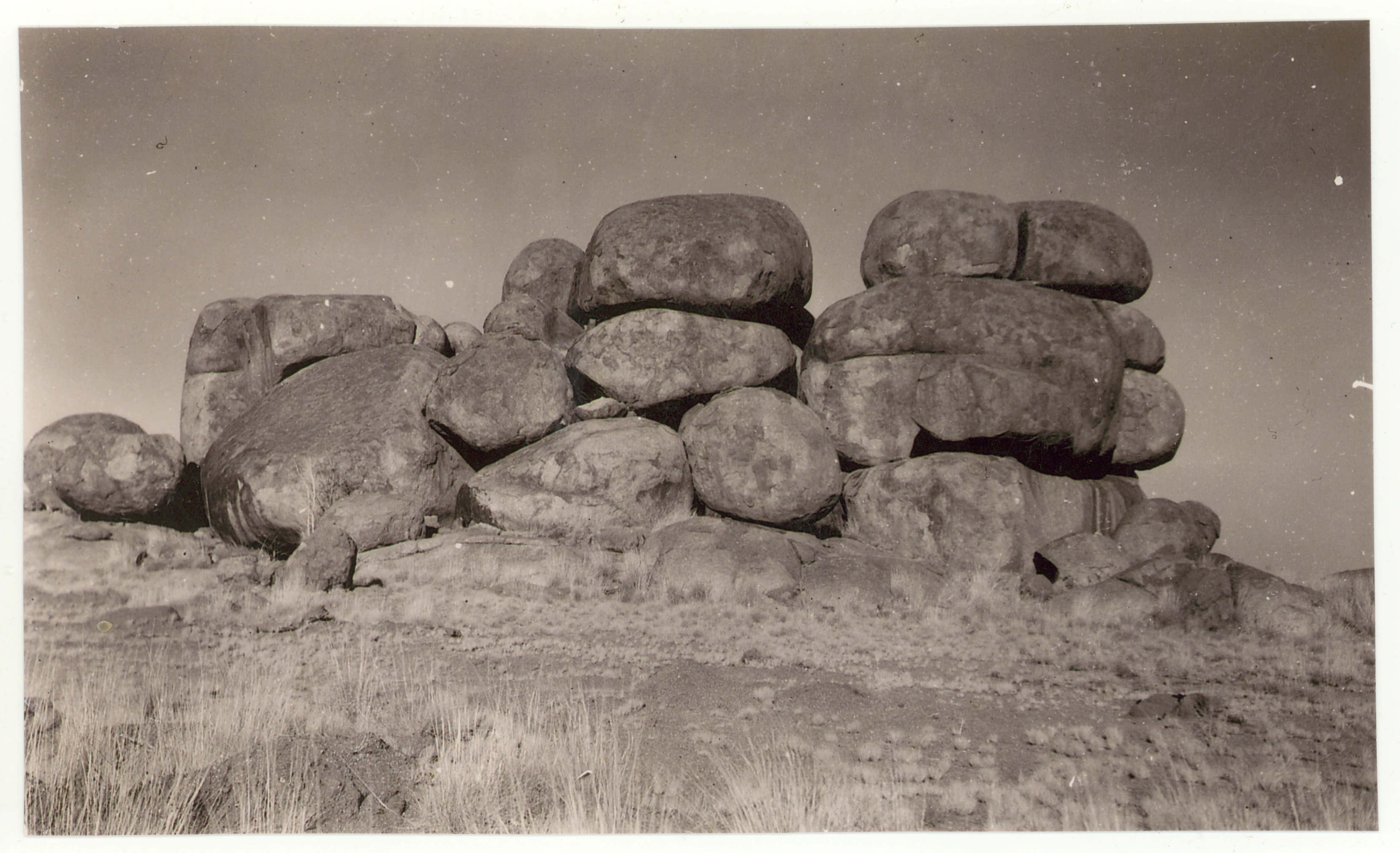 A black and white archival photograph of large, rounded granite boulders stacked naturally in a dry, sparse landscape.