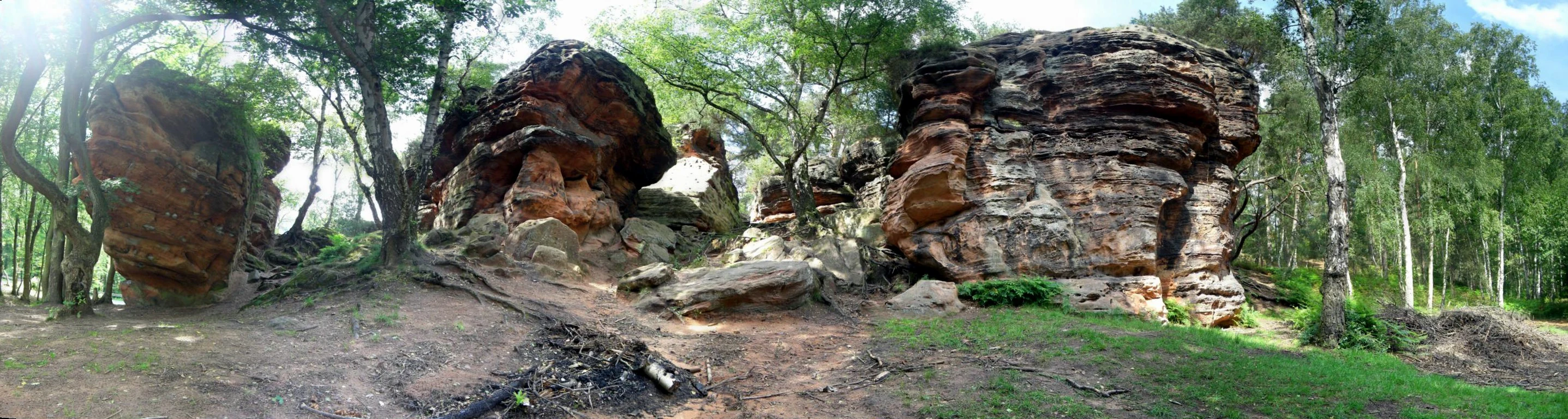 Una toma panorámica de gran angular de varias torres de arenisca grandes y erosionadas, rodeadas por un bosque de árboles caducifolios verdes.