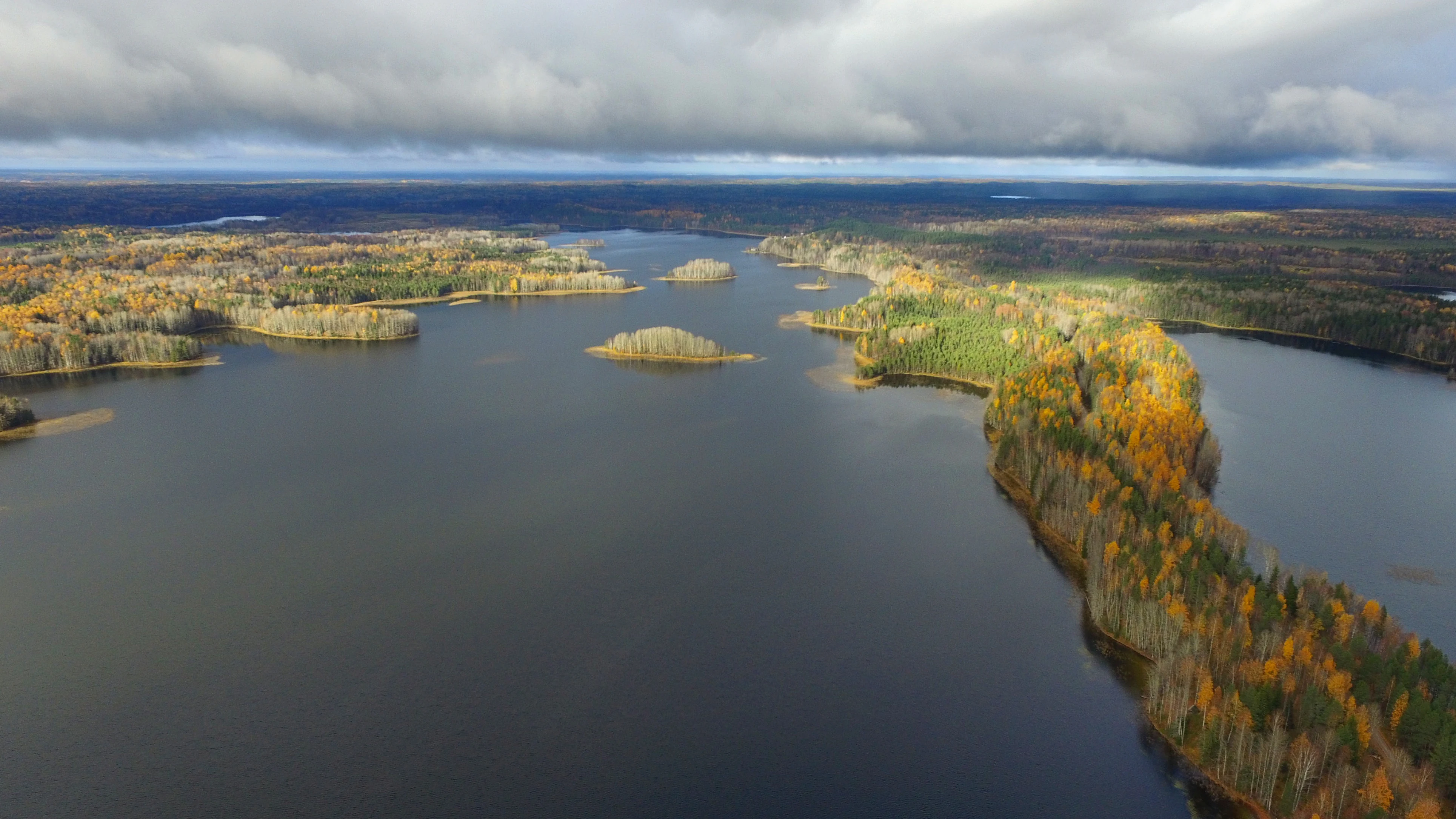 Aerial view of a lake with islands and forested ridges under a cloudy sky
