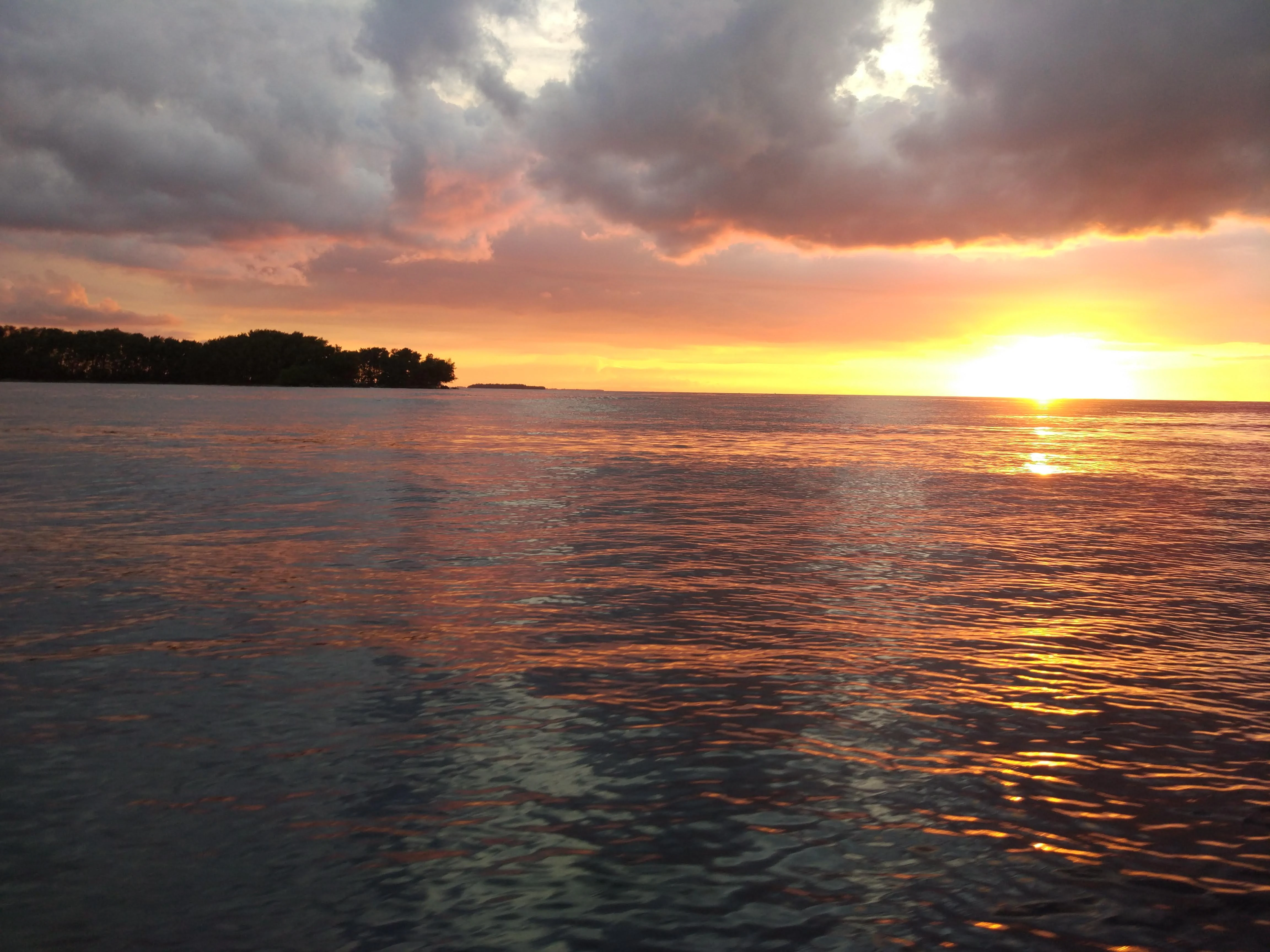 Sunset over water with dramatic clouds and a small island silhouette on the horizon