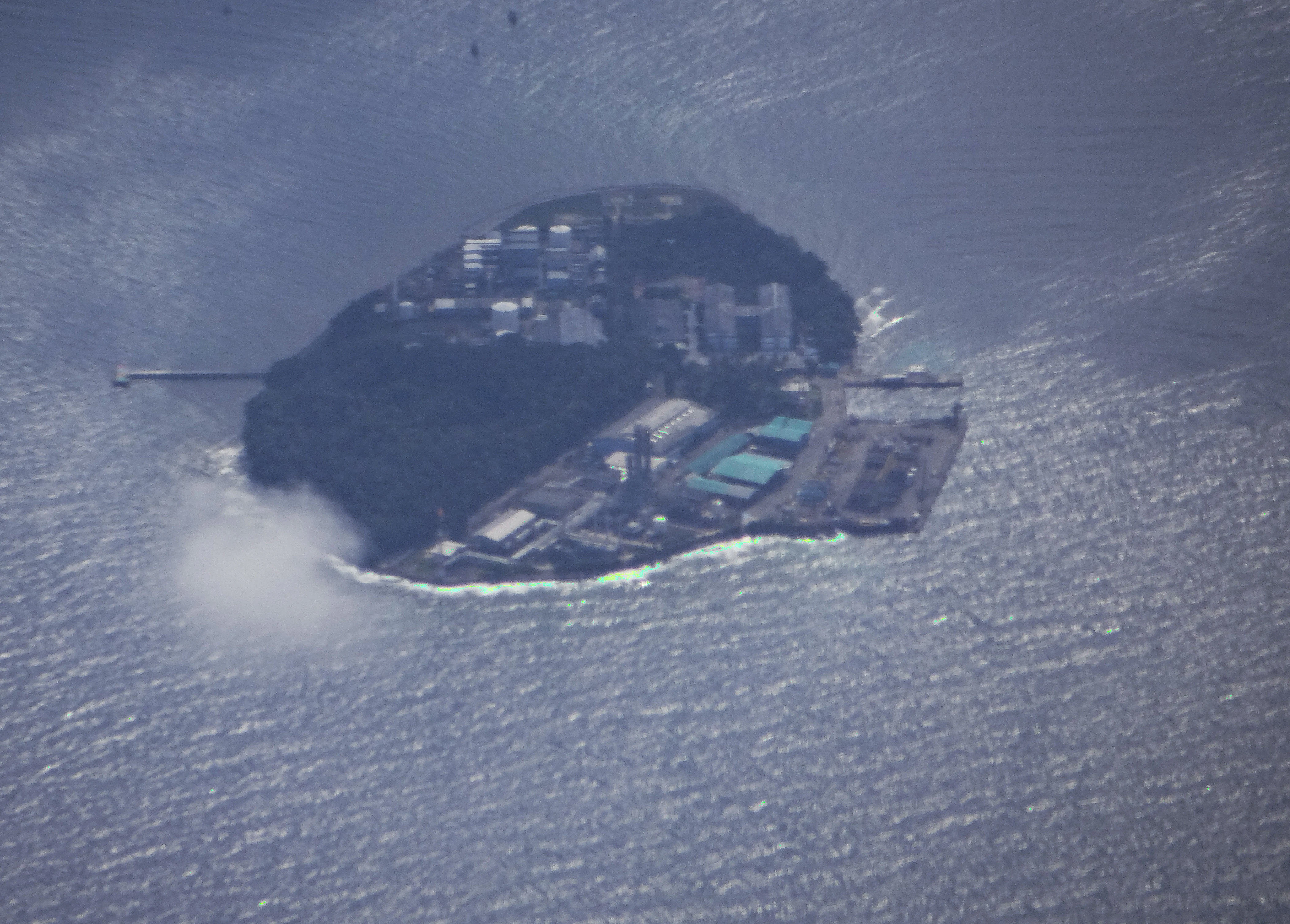 Aerial view of Pabelokan Island showing dense vegetation, buildings, and surrounding water with a small cloud near the shore