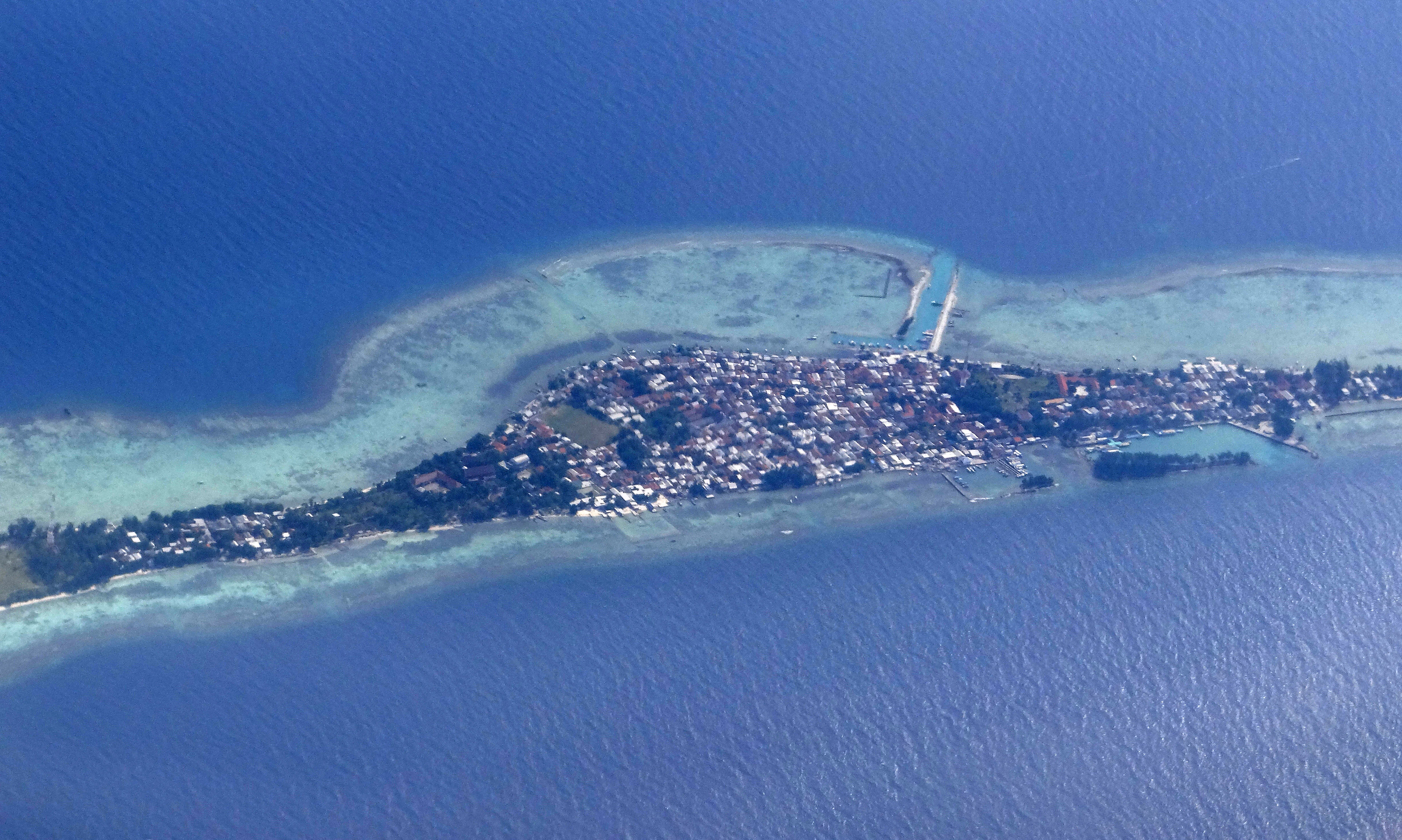 Aerial view of a coastal settlement surrounded by coral reefs and blue water