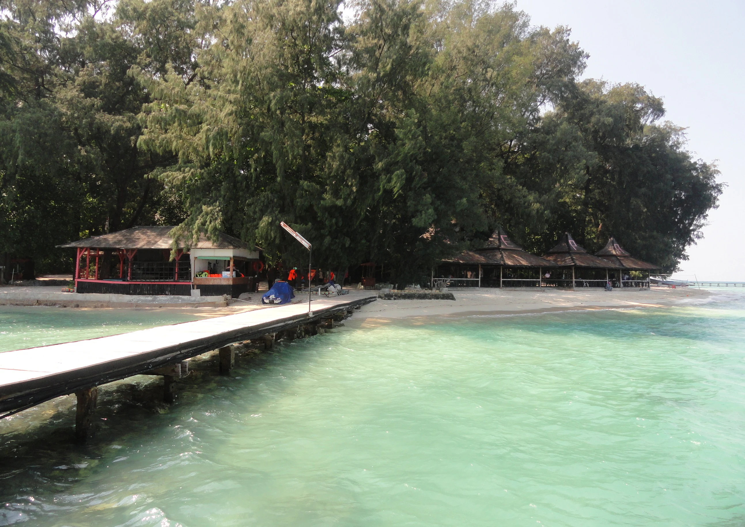 Pier extending into turquoise water with resort buildings and trees on Pulau Sepa, Indonesia