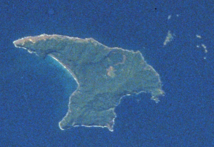 An aerial or satellite photograph of the volcanic Raoul Island surrounded by deep blue ocean water.