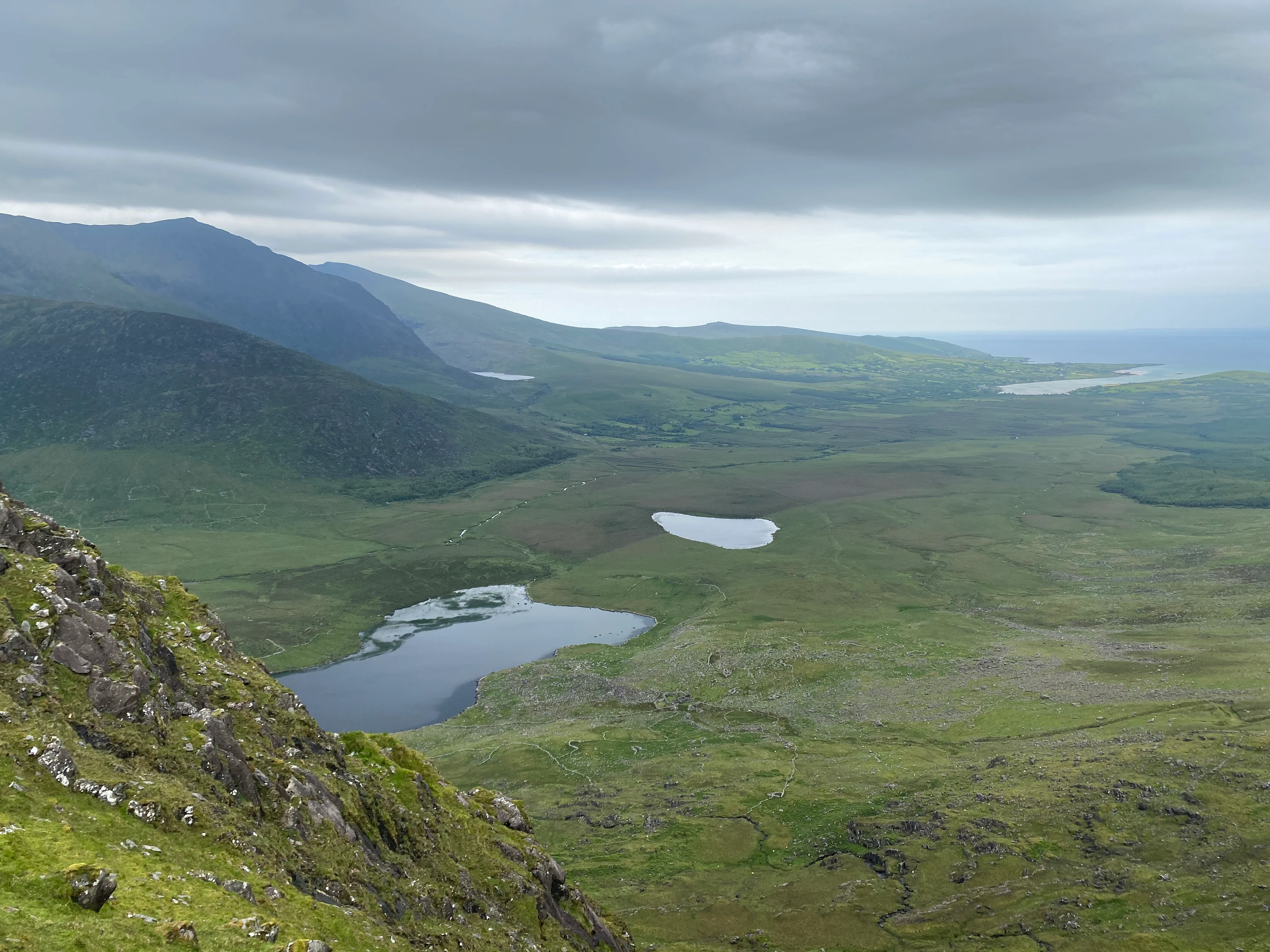Green hills, two lakes, and mountains under cloudy sky in Conor Pass, County Kerry