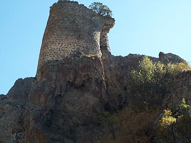 Ancient stone fortress tower ruins perched on a rugged cliff edge against a clear blue sky.