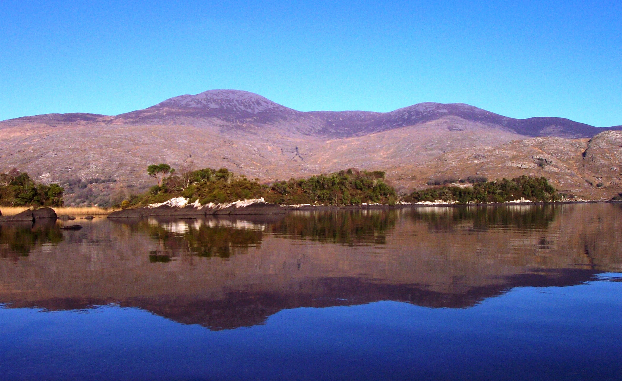 A calm lake reflecting mountains under a clear blue sky