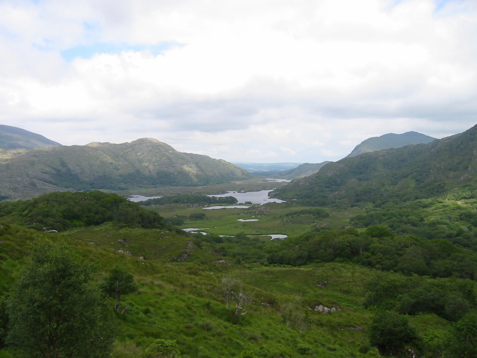 Wide landscape view of the Lakes of Killarney with green hills, mountains, and a partly cloudy sky