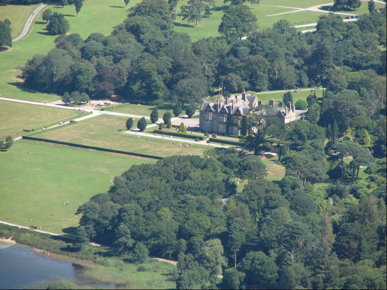 Aerial view showing Muckross House surrounded by green fields and forests with a lake visible in the lower left corner