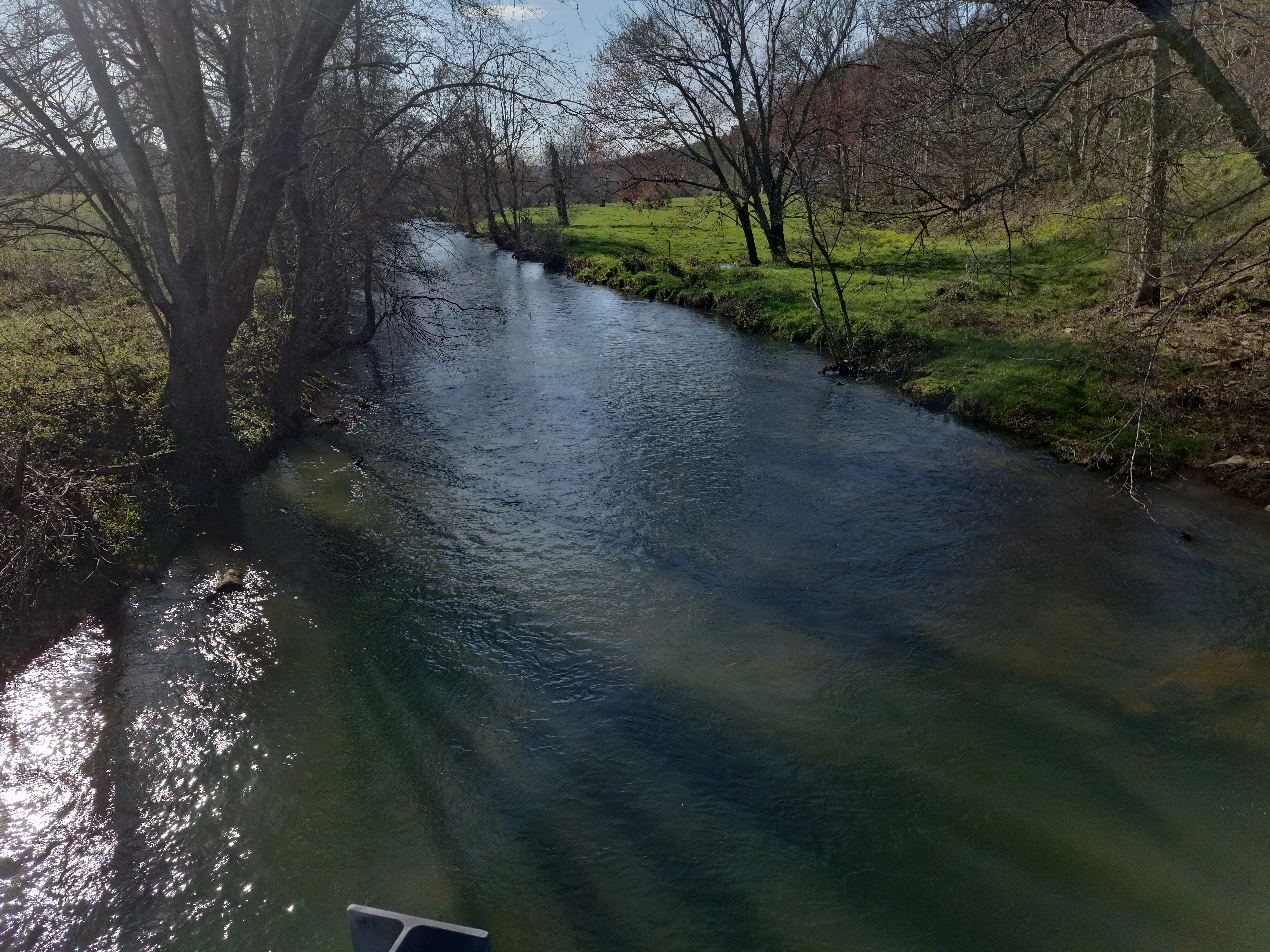 A view of Kimberling Creek flowing through a rural valley, flanked by trees and green fields.