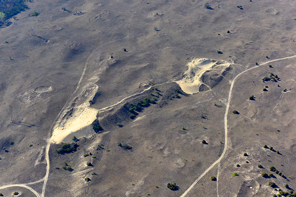 Aerial view showing sand dunes with winding paths and sparse vegetation in a flat, arid landscape