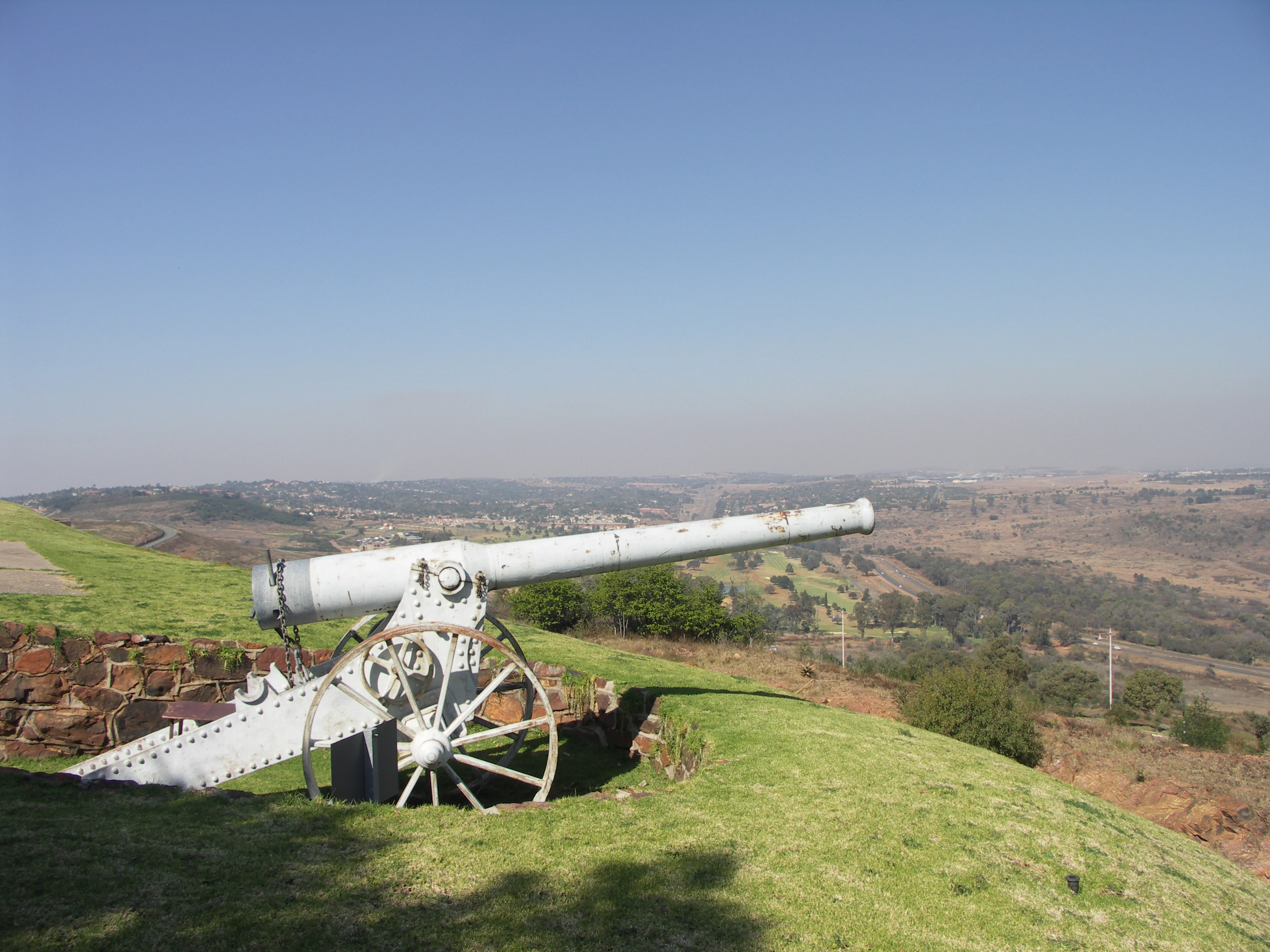 A metal Long Tom cannon replica sits on a grassy hill overlooking a valley.