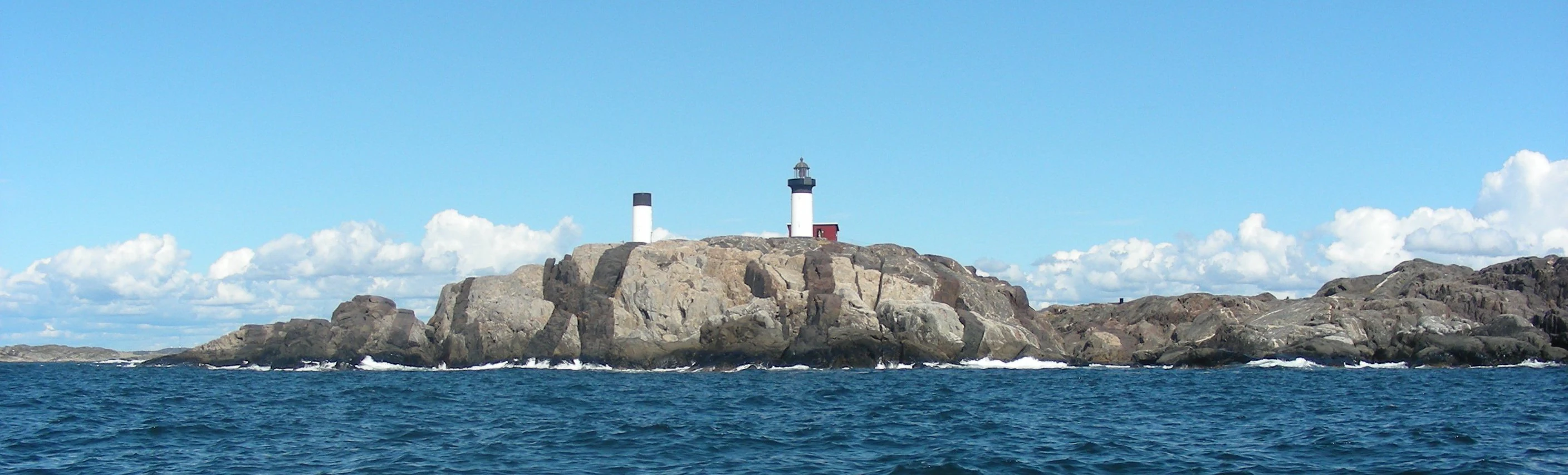 A coastal scene featuring two lighthouses on a rocky island with the sea in the foreground and a clear sky