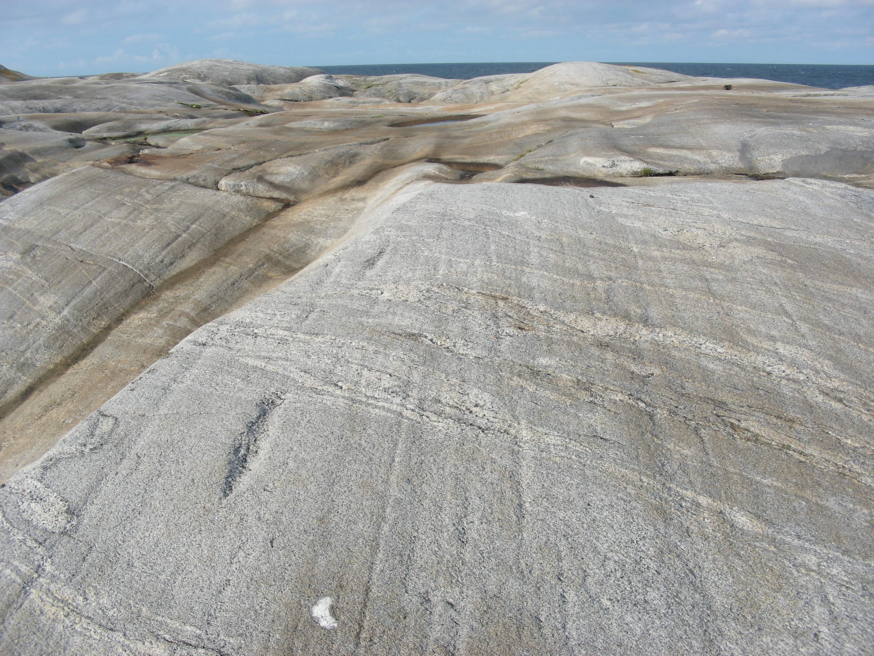 Rocky terrain with linear glacial scratches and grooves, distant sea horizon under clear sky