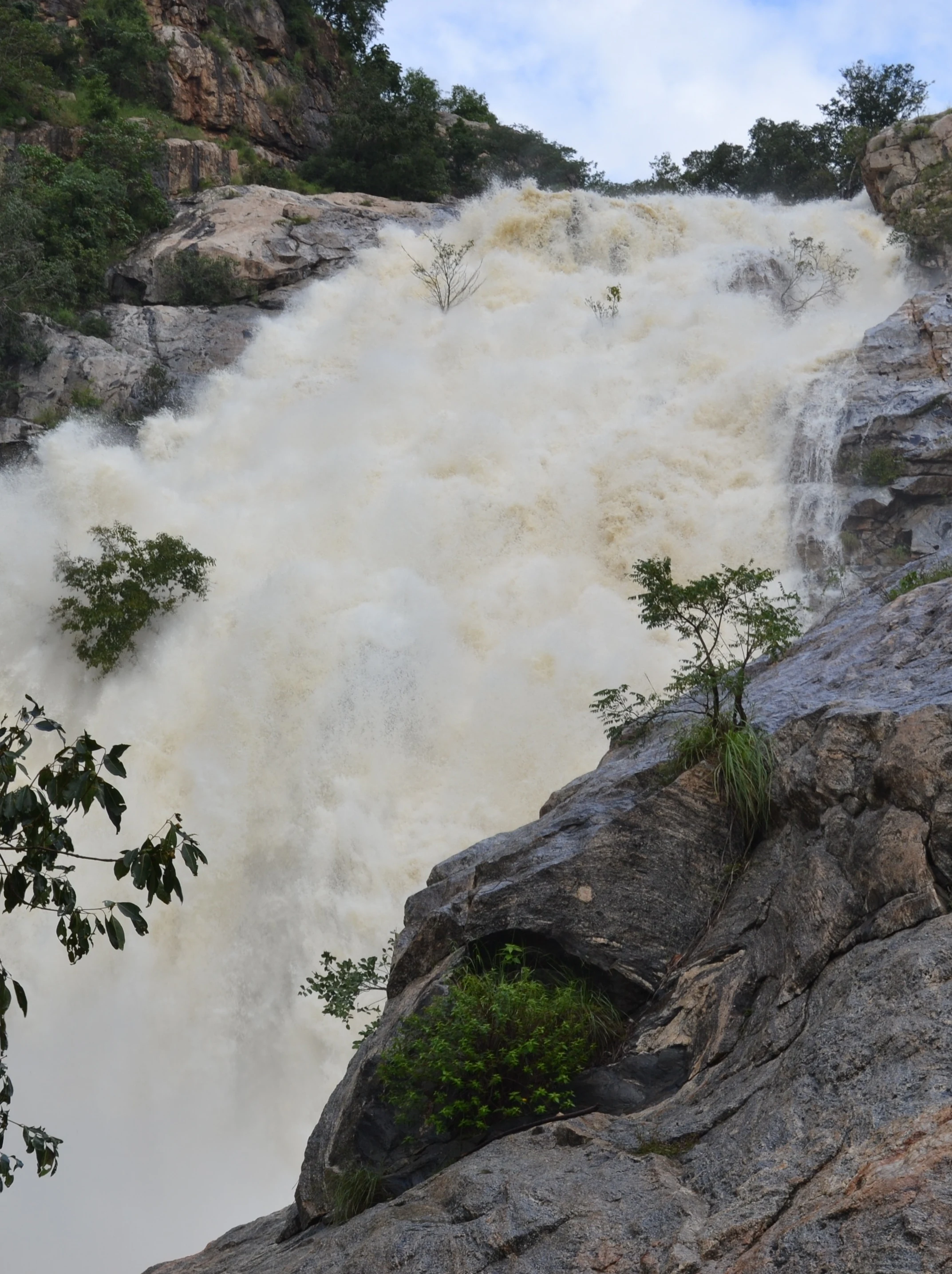 A close view of a large, powerful waterfall cascading over rugged rocky cliffs, surrounded by patches of vegetation.