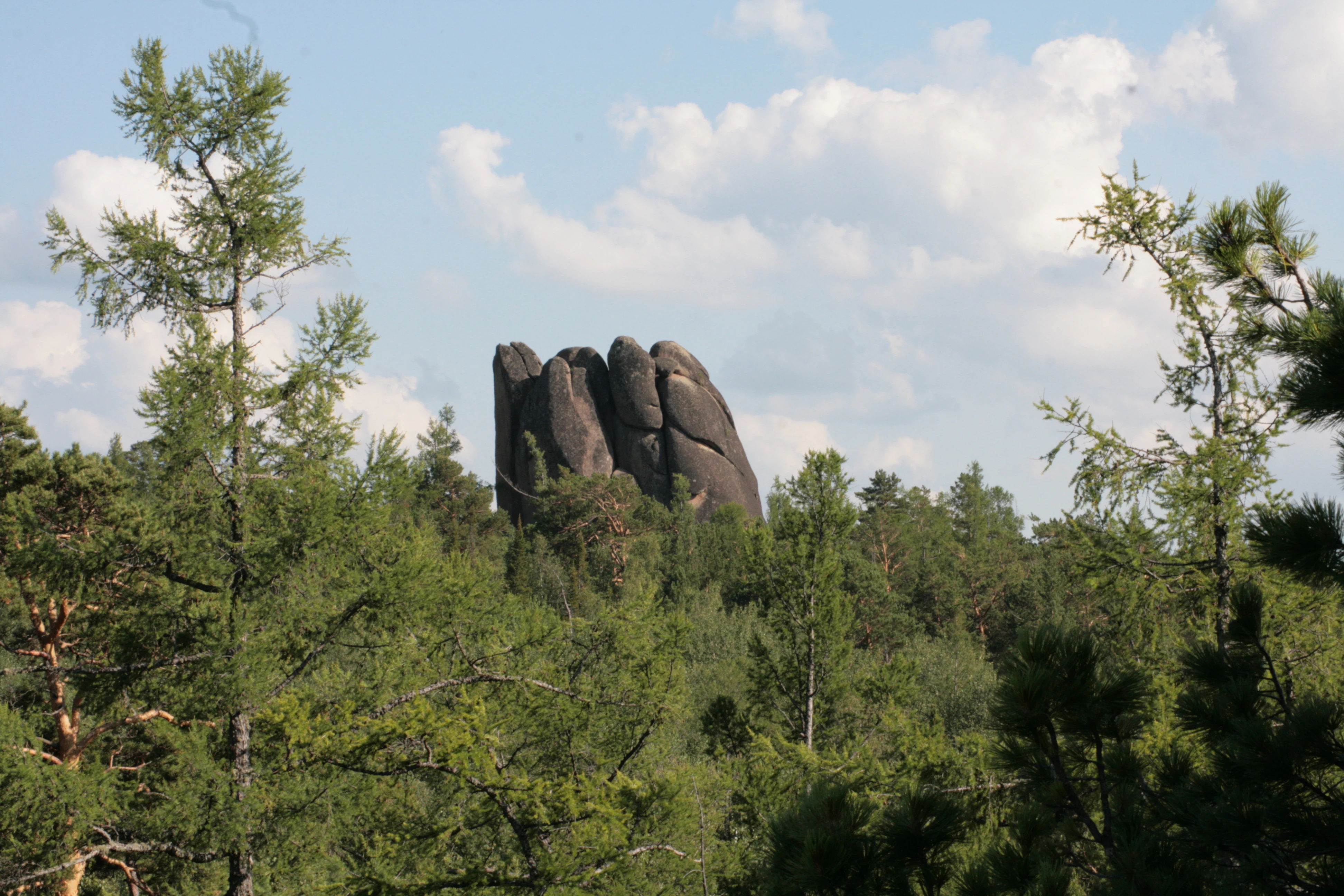 Tall dark rock formations rising above dense green forest under a partly cloudy sky