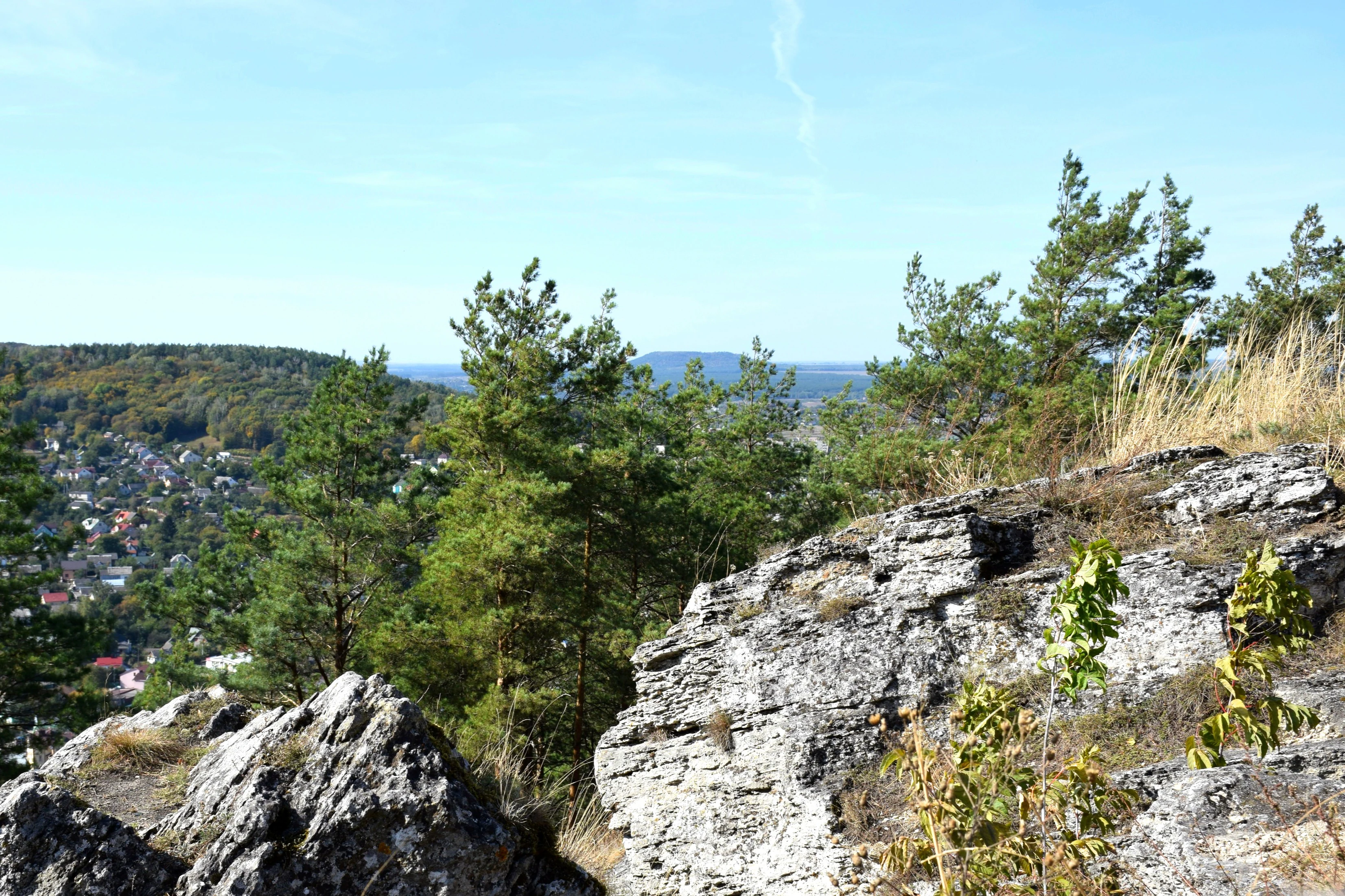Rock formations on Devi Skeli mountain, forested landscape, distant town under clear sky