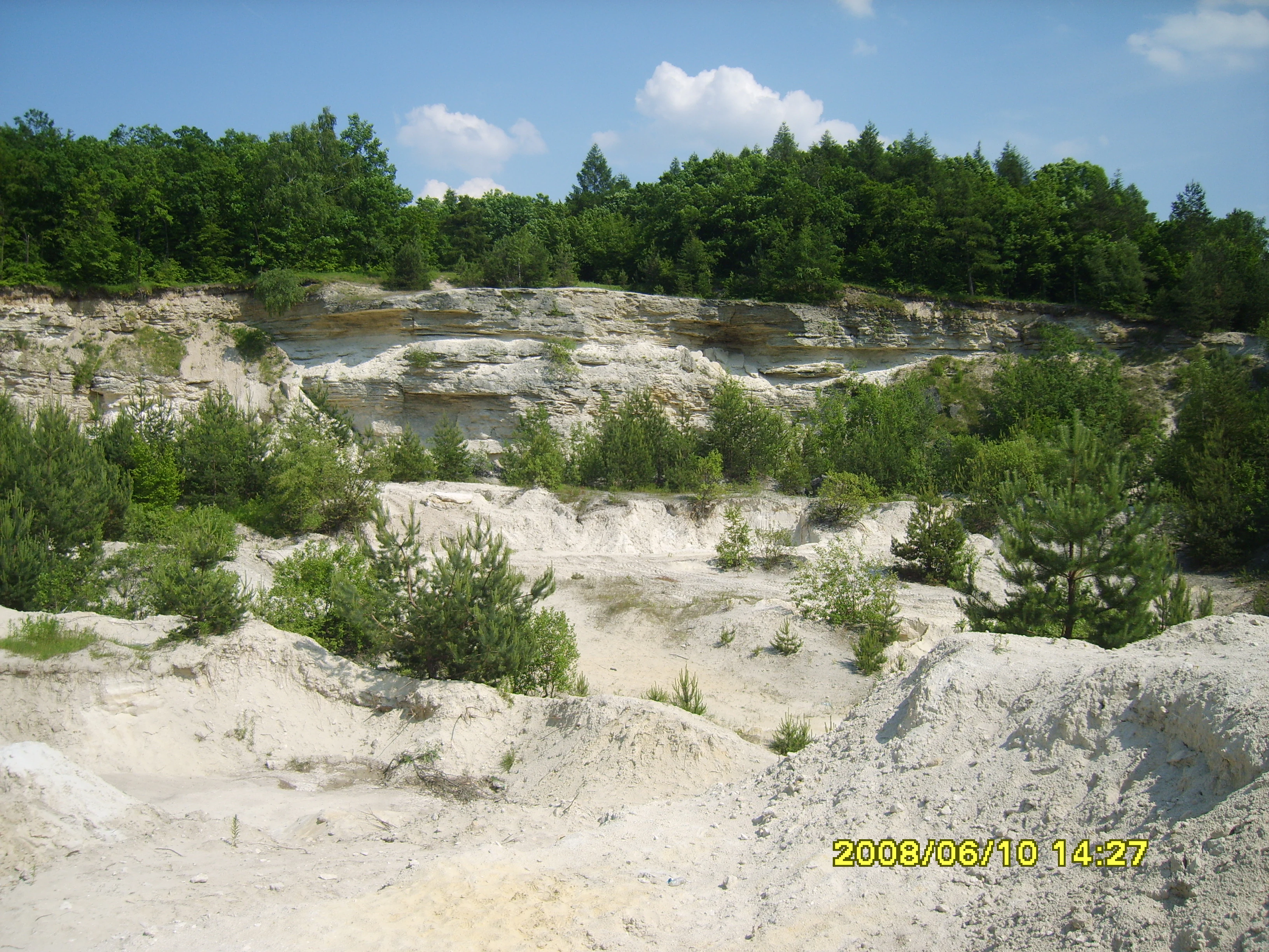 Landscape view of layered rock formations with green vegetation under a partly cloudy sky