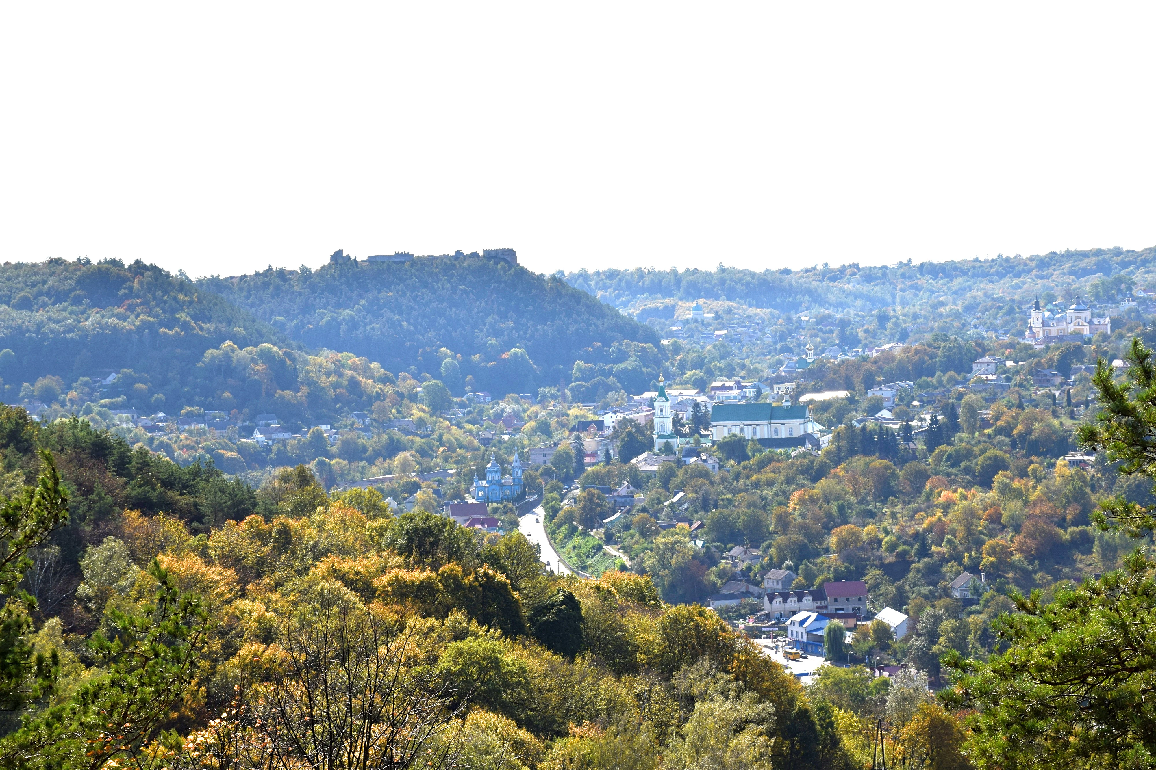 Wide landscape view of Zamkova Hora mountain with the town of Kremenets below, surrounded by autumn-colored trees and rolling hills under a bright sky