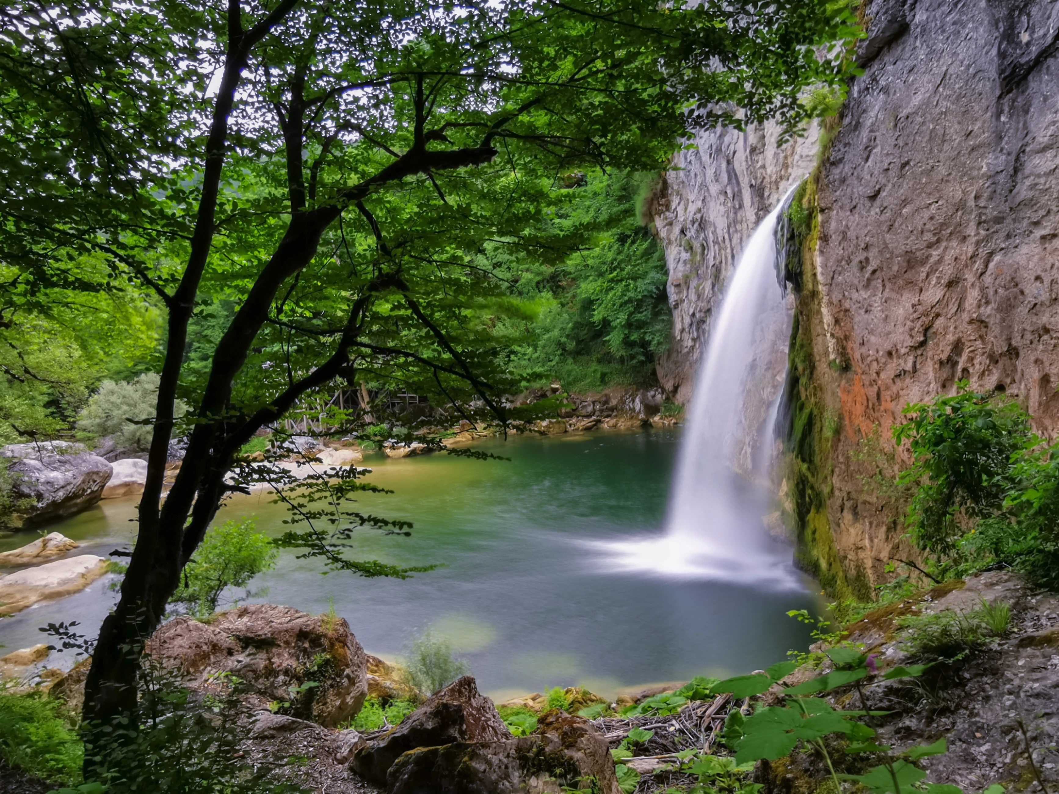 Waterfall flowing into a calm pool surrounded by rocky terrain and dense green foliage