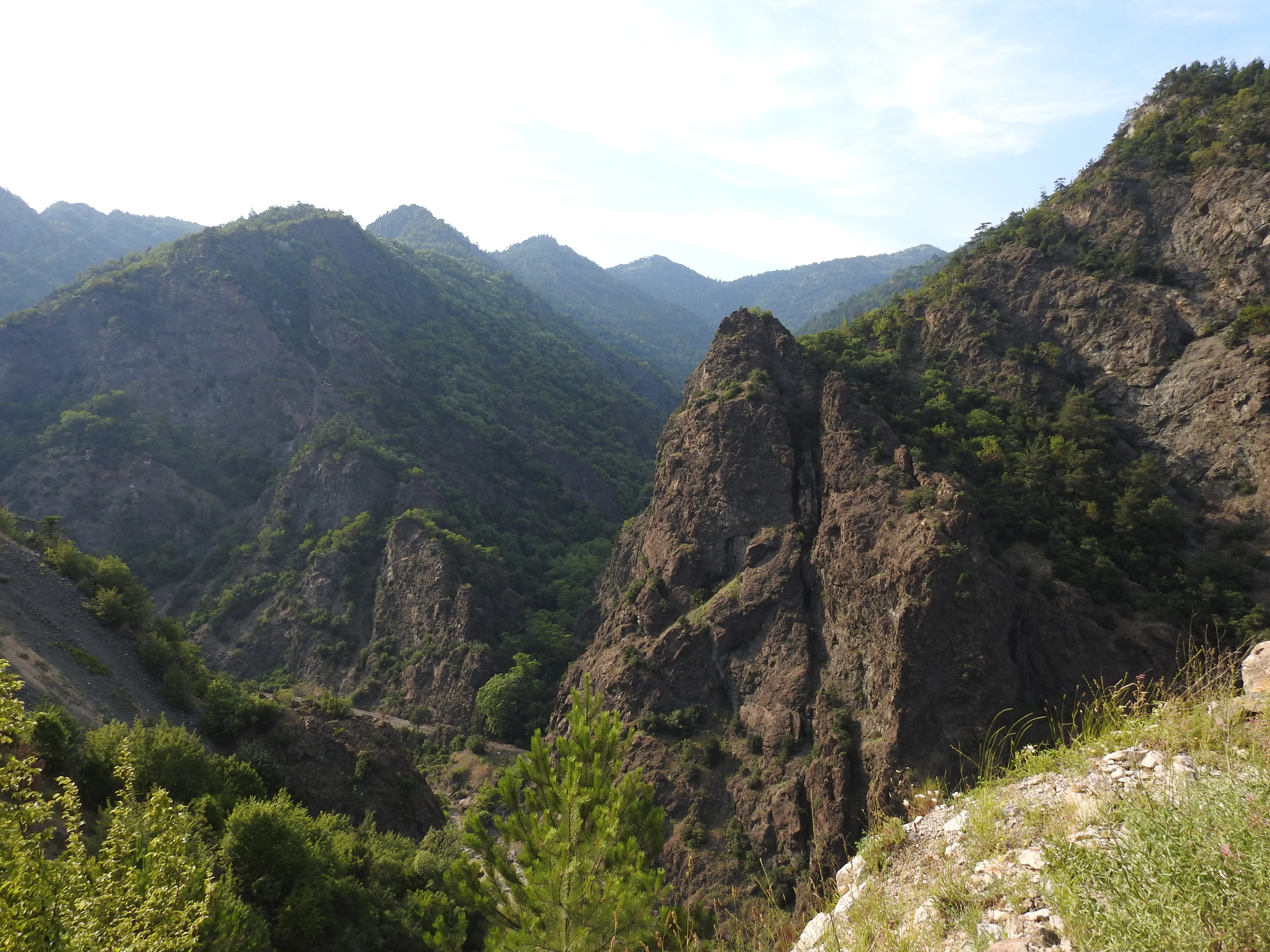 Mountainous landscape with rocky peaks, valleys, and green vegetation under a partly cloudy sky.