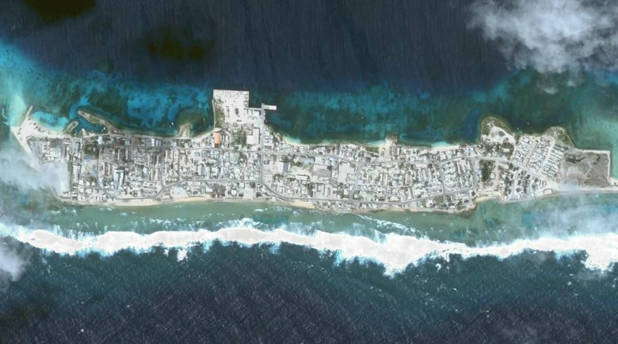 Vista satelital cenital de una isla estrecha y densamente urbanizada rodeada de aguas oceánicas turquesas y azul profundo, que muestra una estructura urbana distintiva y formaciones de arrecifes.