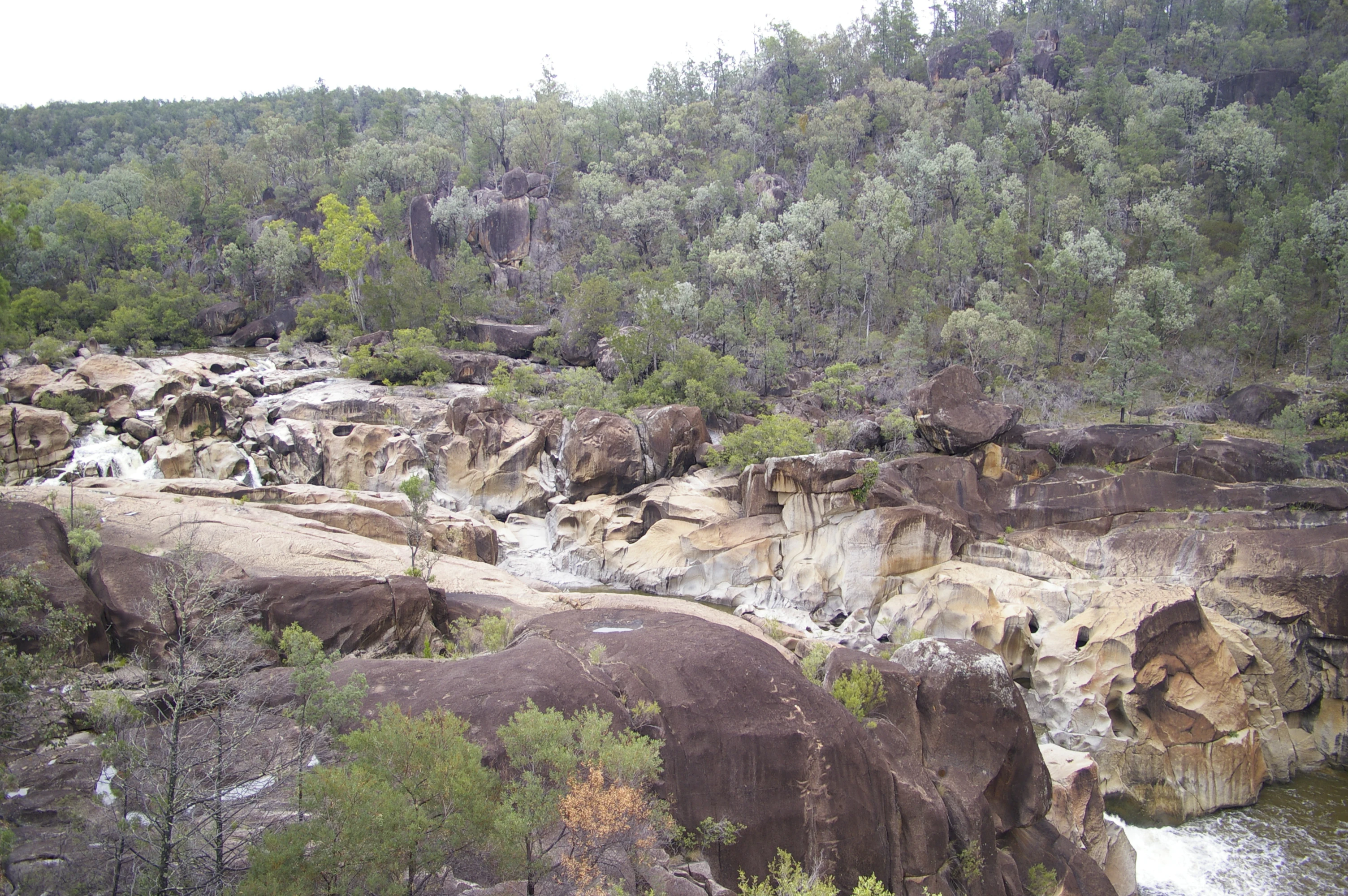 Una vista panorámica de las cataratas MacIntyre, que muestra agua fluyendo sobre grandes rocas con colinas boscosas al fondo