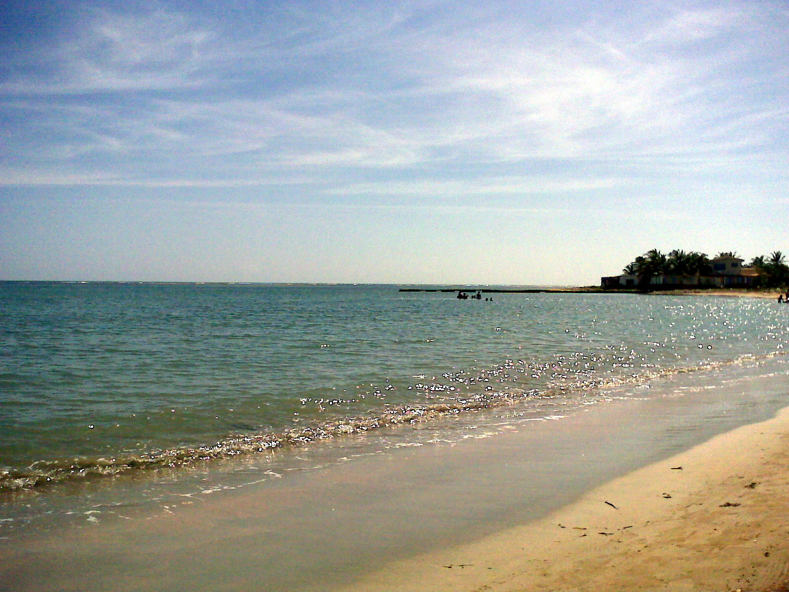Sandy beach with calm turquoise water extending to the horizon under a partly cloudy sky