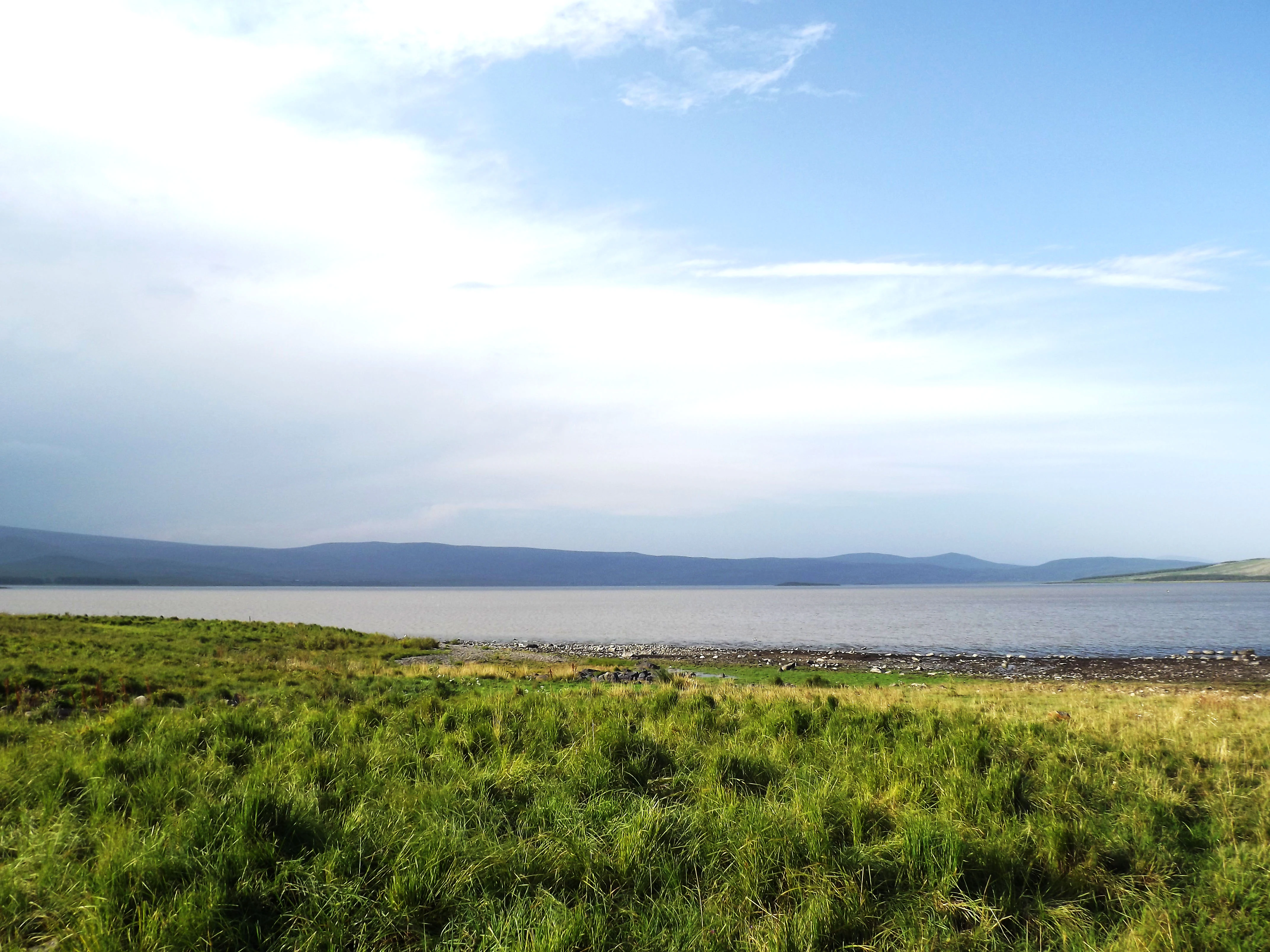 Grassy field extending to Lake Arpi with mountains in the background under a partly cloudy sky