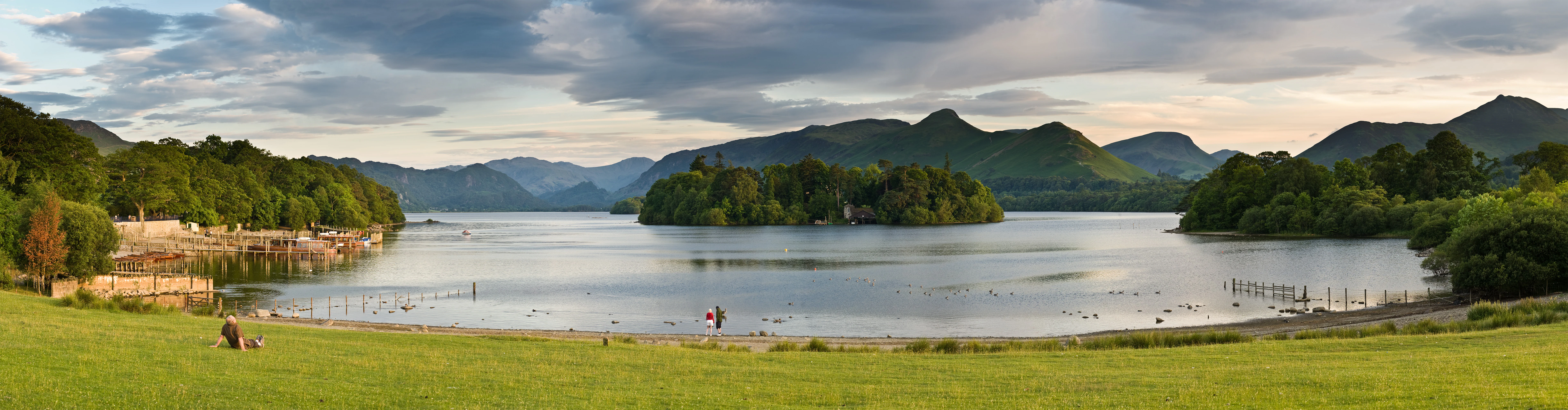Derwent Water lake with green hills, grassy shore, and people walking